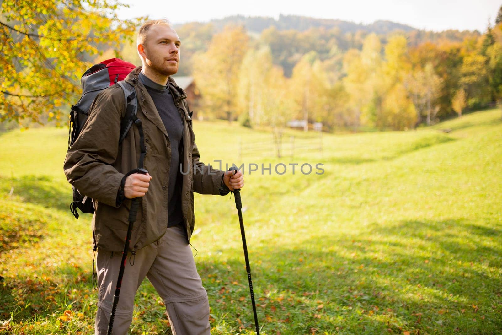 Portrait of a male adventurer hiking in the mountains with a backpack and trekking sticks in his hands standing on a mountain and looking to the side. Hiking. Banner. Place for advertising or text.