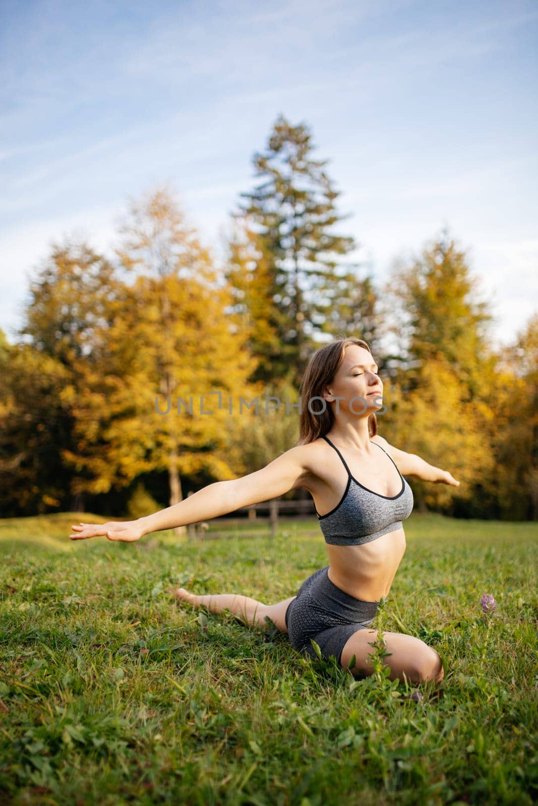 Young woman in sportswear practicing yoga and meditation doing breathing exercises outdoors outside the city. Woman trains on the grass in the morning. Concept of a healthy lifestyle and relaxation.