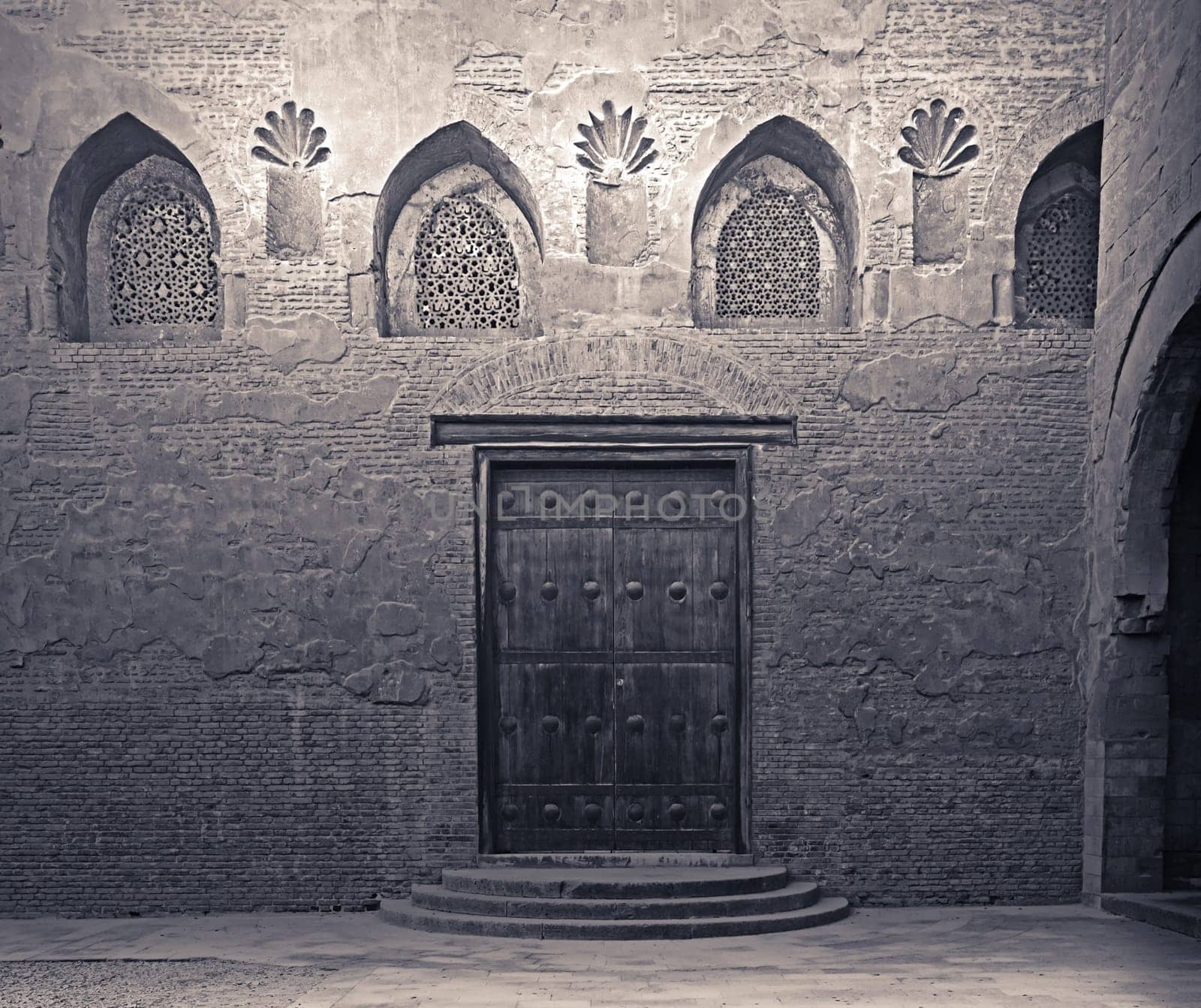 Aged wooden weathered door, perforated arched stucco window decorated with floral patterns, and three steps on stone bricks wall, Ibn Tulun Mosque, Cairo, Egypt