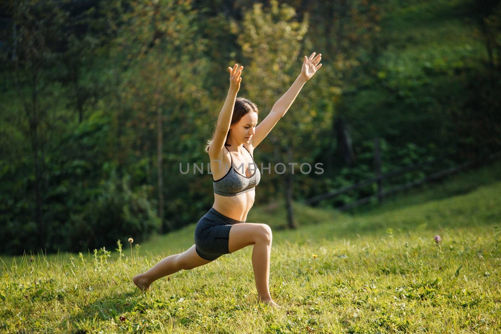 Young woman in sportswear practicing yoga and meditation doing breathing exercises outdoors outside the city. Woman trains on the grass in the morning. Concept of a healthy lifestyle and relaxation.
