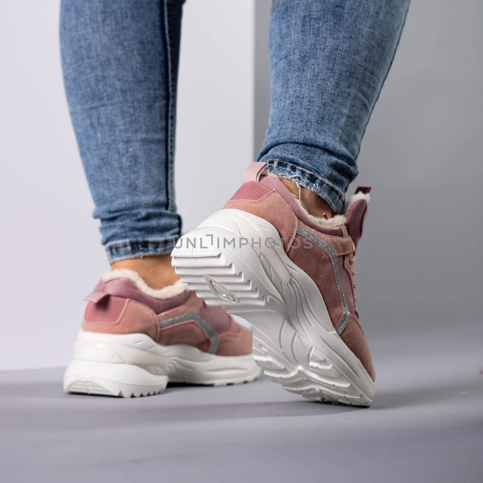 Close up demonstration of rear view of female model in warm sneakers with down inside. Comfortable white and pink sneakers on woman's legs in jeans. Selective focus.