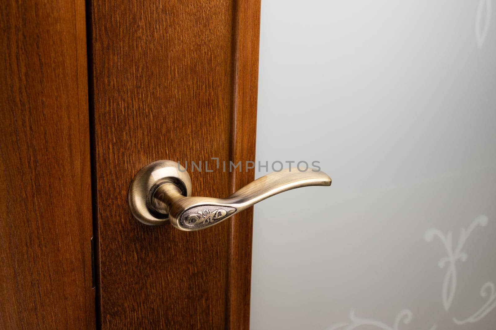 External door handle without protective lock on wooden frame. Close up of gold door handle on brown front or interior door. Home door design choice concept.