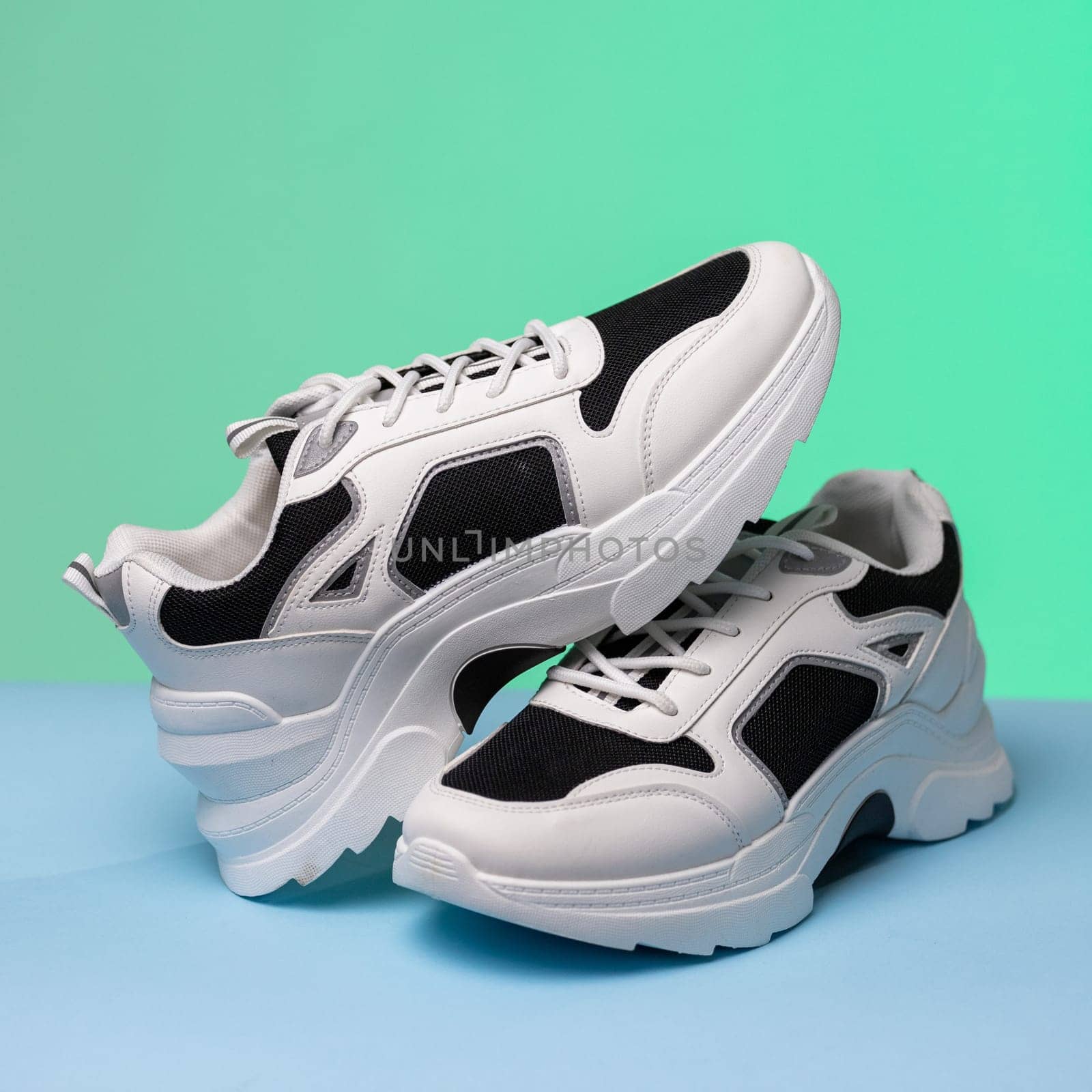 Details. Close up of black and white sports shoes on colored background. One sneaker rests on another standing on blue and green background. Sports shoe store concept. Banner. Copy space.
