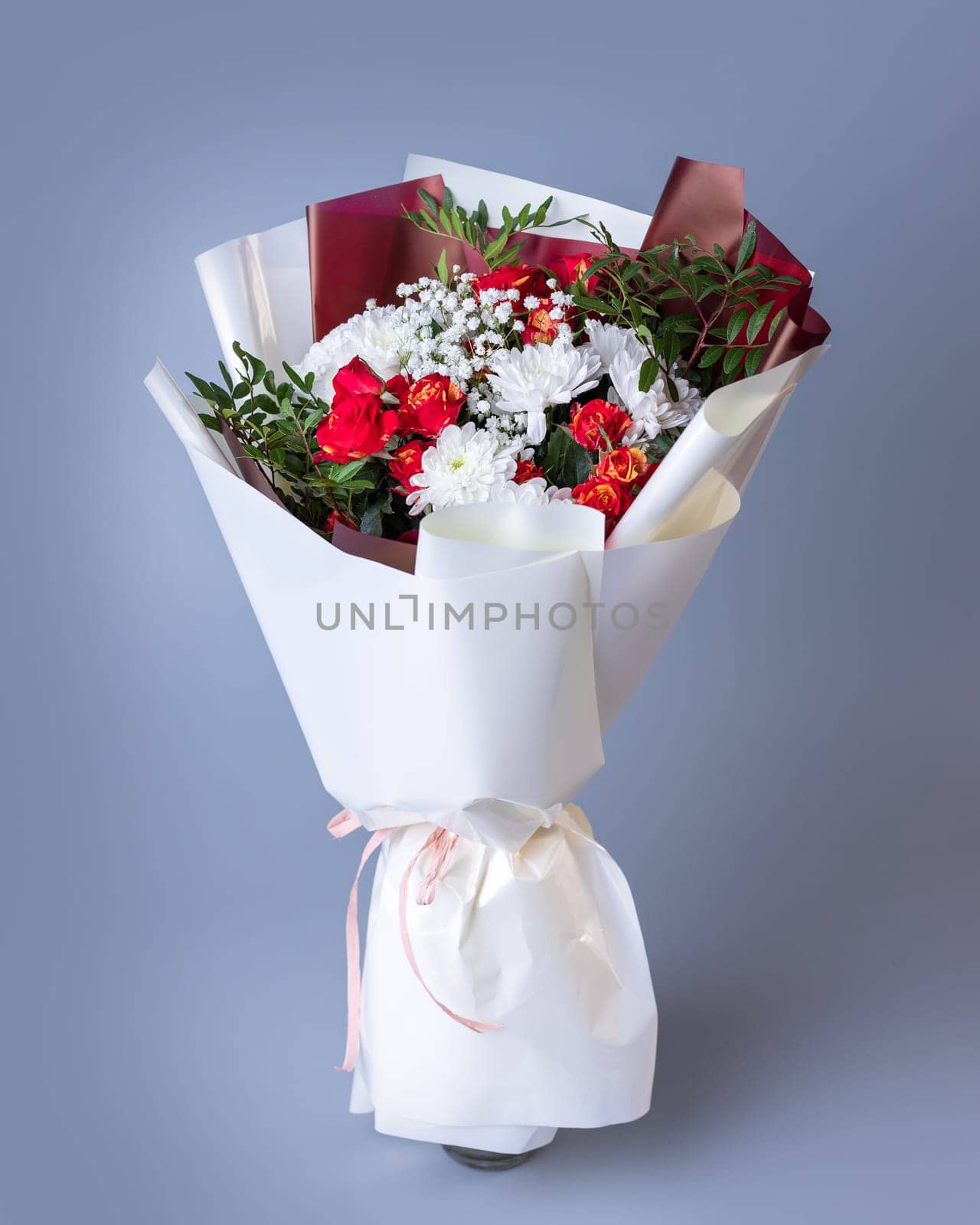 White and red flowers wrapped in bright floral paper on a blue background. Festively packed bouquet of pink roses, white chrysanthemums, gypsophila and sprigs of greenery.