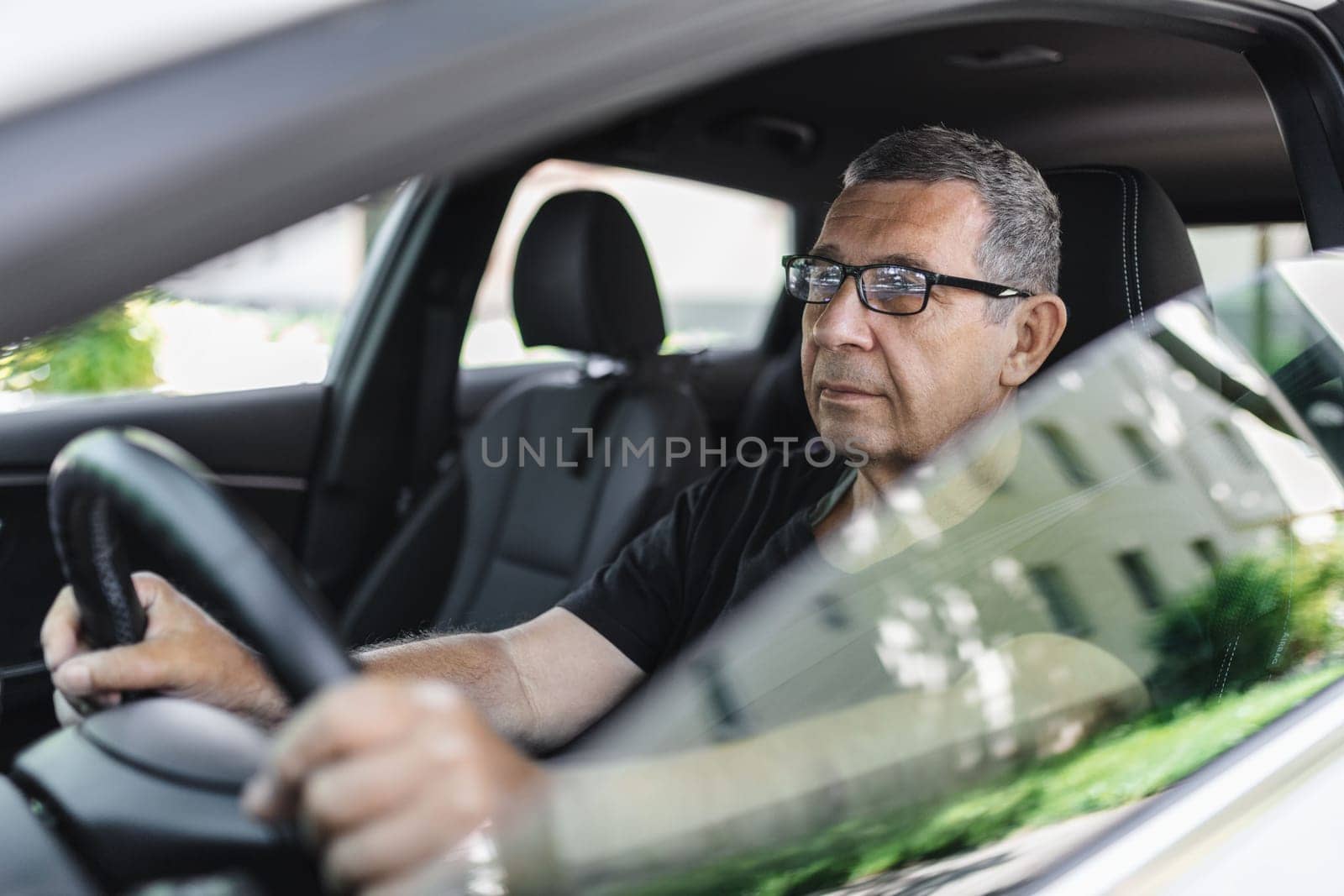 Happy senior in his 70s driving a car