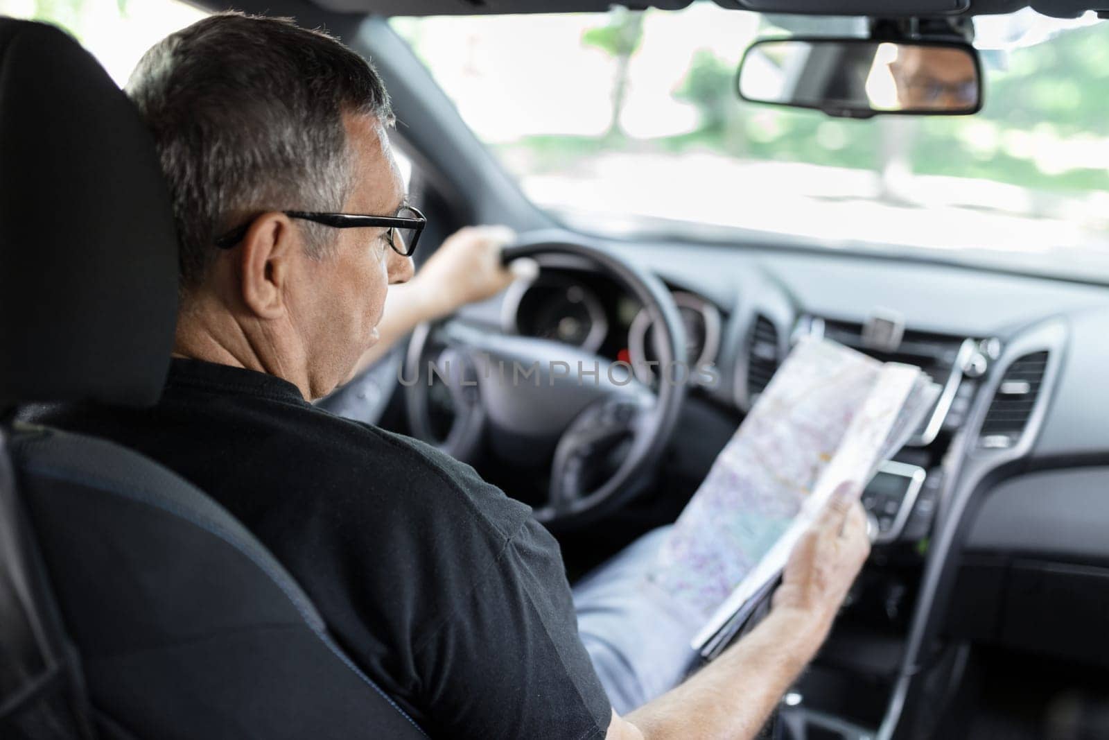 Senior behind the steering wheel of a car, looking at map for directions