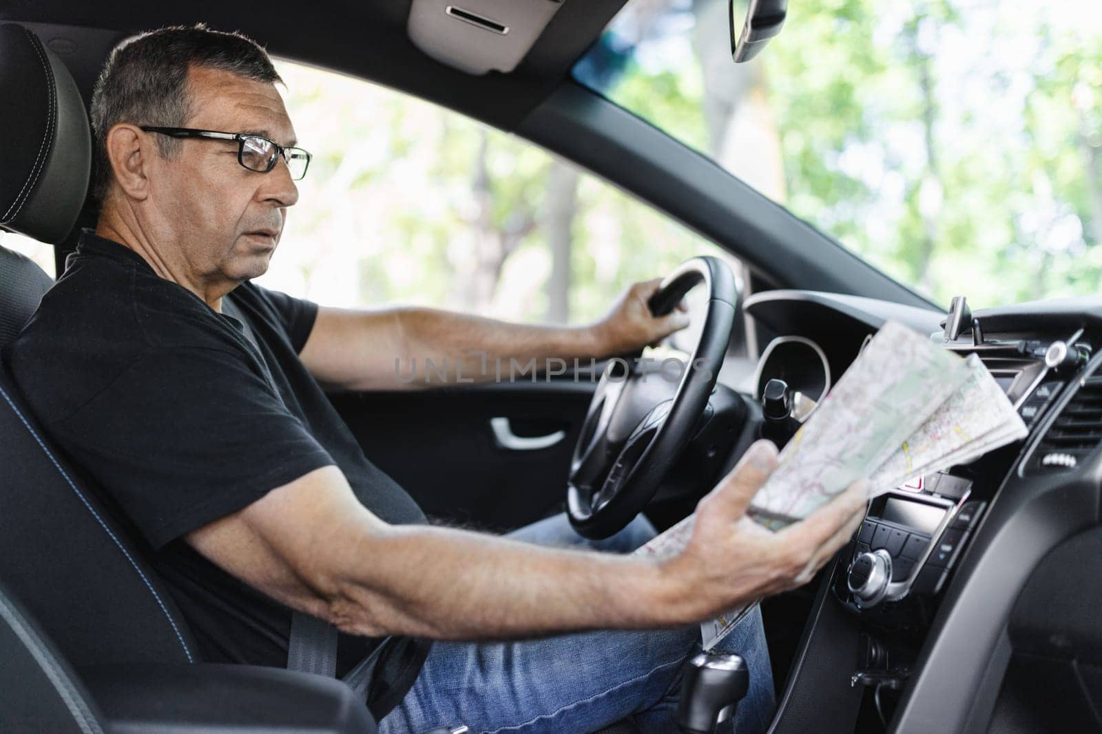 Senior behind the steering wheel of a car, looking at map for directions