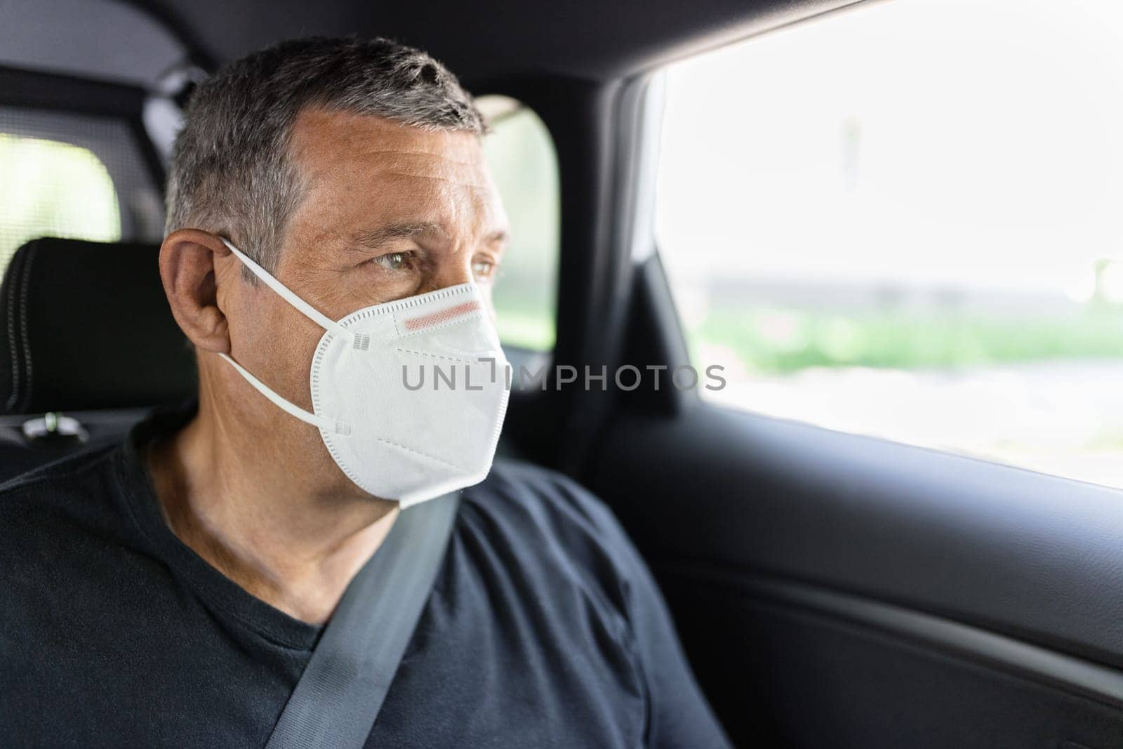 Senior in his 70s sitting at the back of car wearing a face mask for protection against corona virus