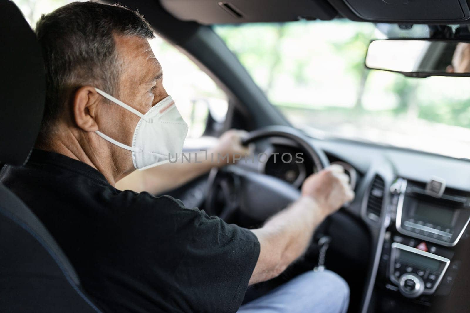 Senior in his 70s driving a car wearing face mask for protection against corona virus
