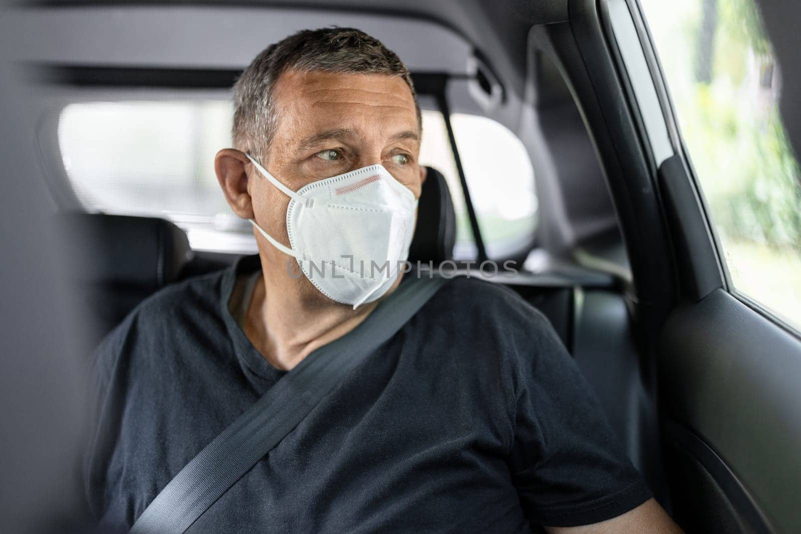 Senior in his 70s sitting at the back of car wearing a face mask for protection against corona virus