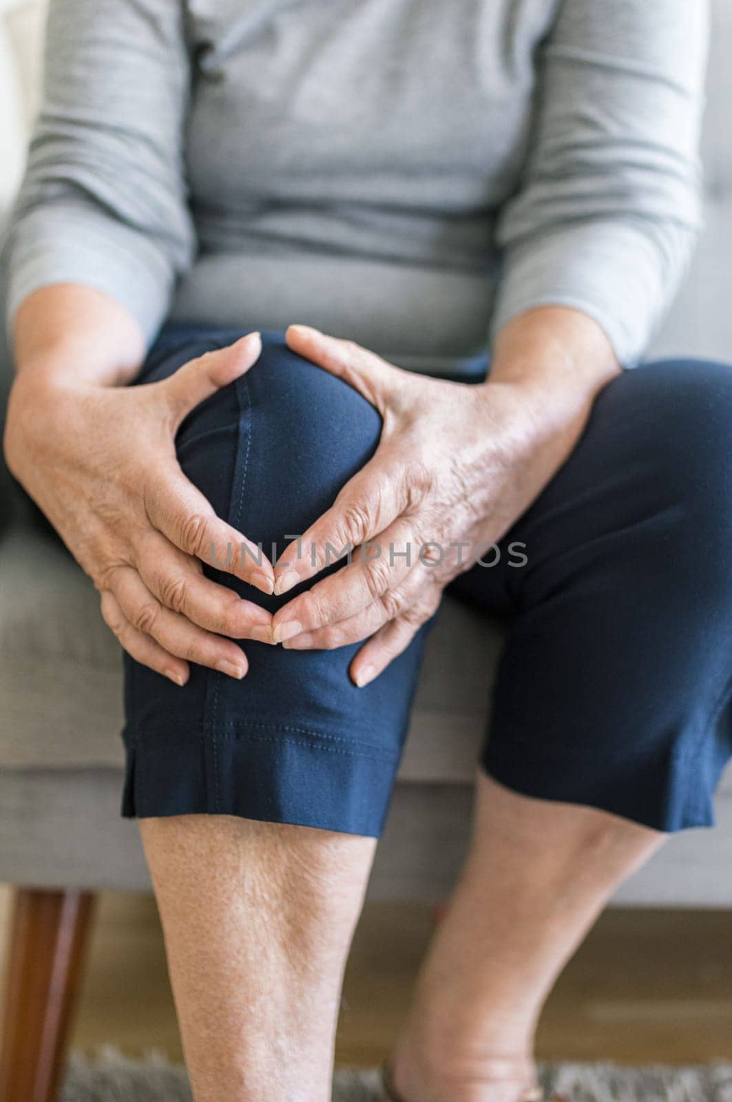 Senior woman sitting on bench, holding her painful knee