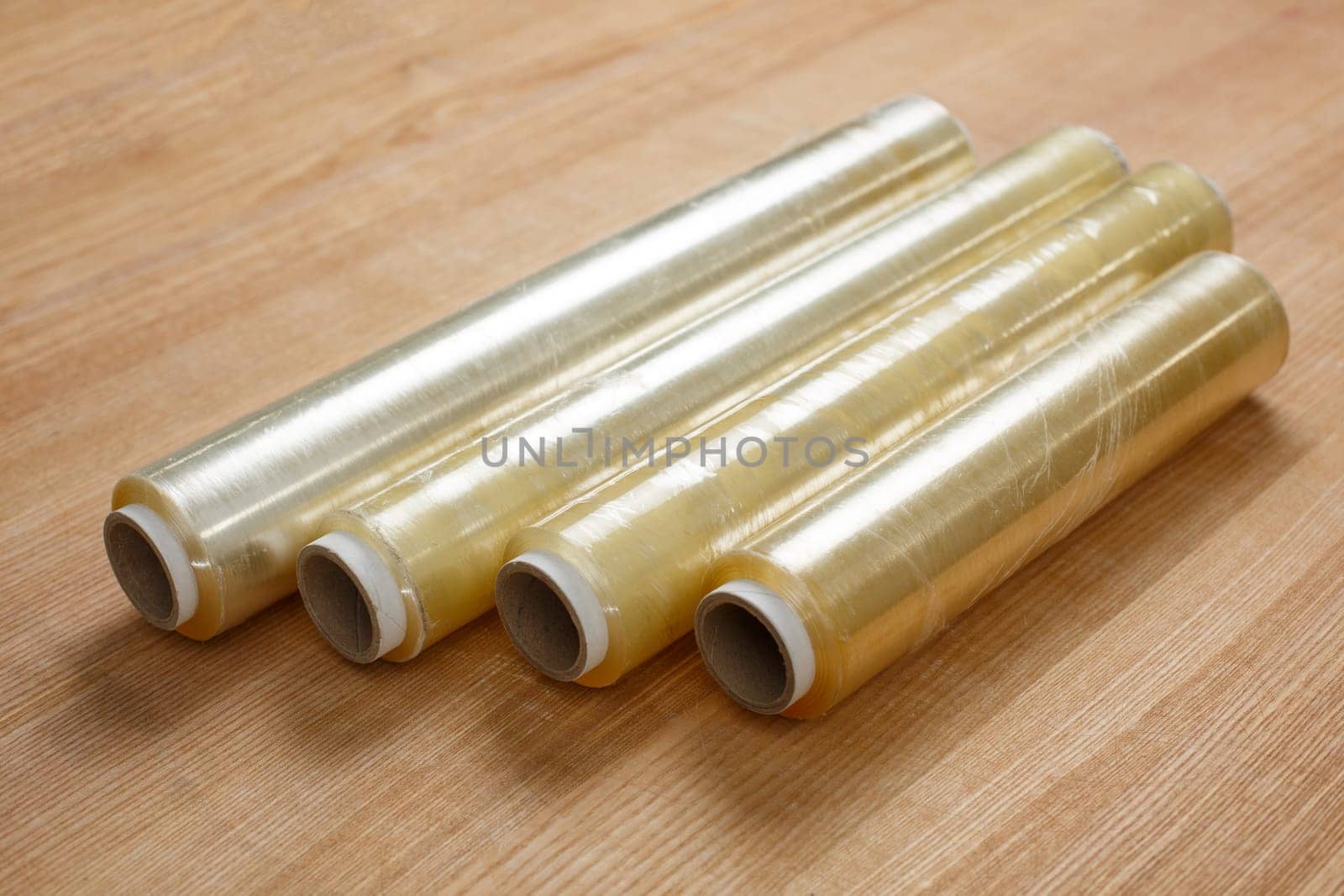 Close up on wooden table lies four rolls of transparent food film on cardboard spool. Concept of product packaging, product storage, damage protection and household packaging.