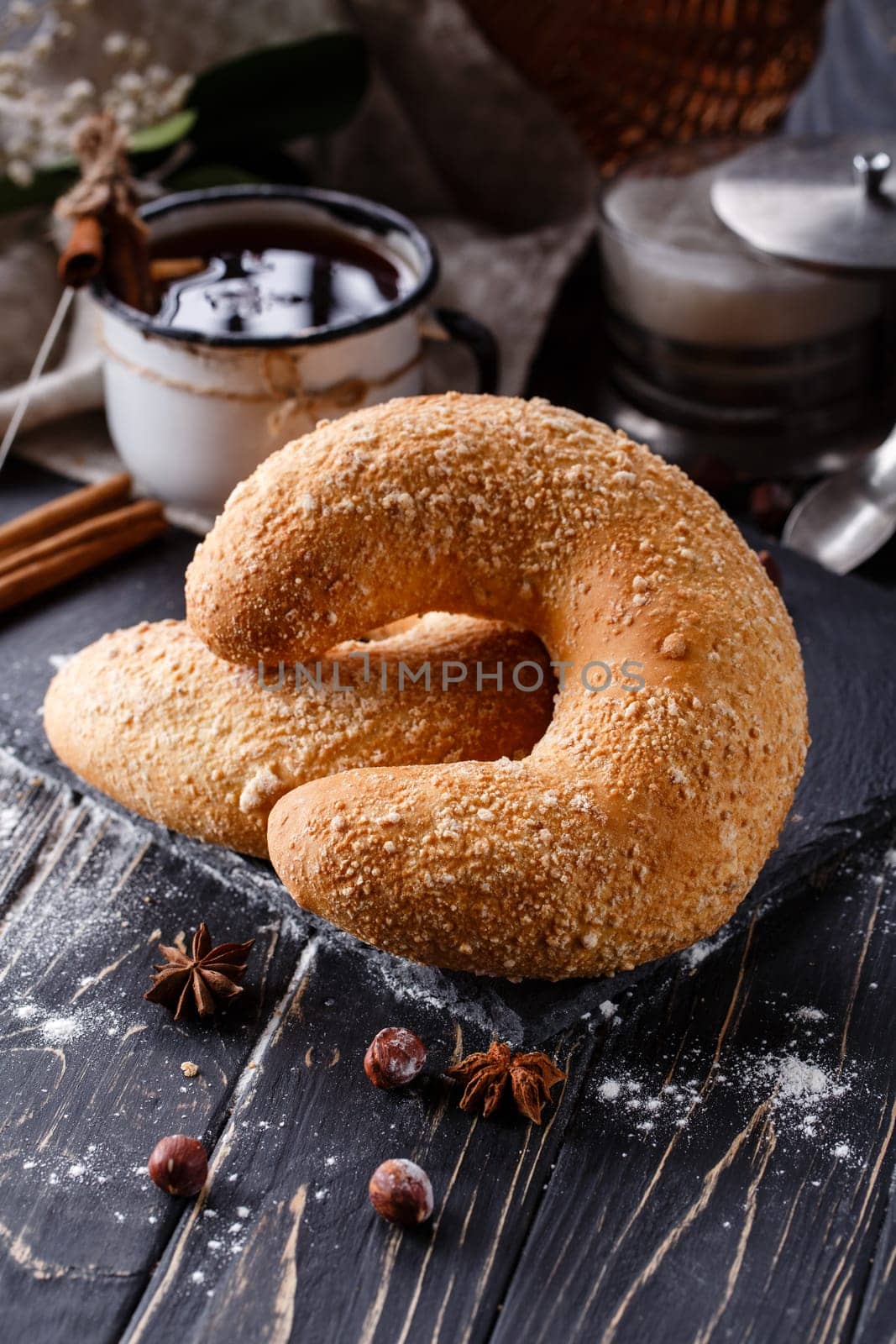 Country home lifestyle. Close up of big sweet bagel on dark rustic wooden table. Crescent-shaped bagels lie near fragrant spices on background of cinnamon sticks and coffee in enamel mug.