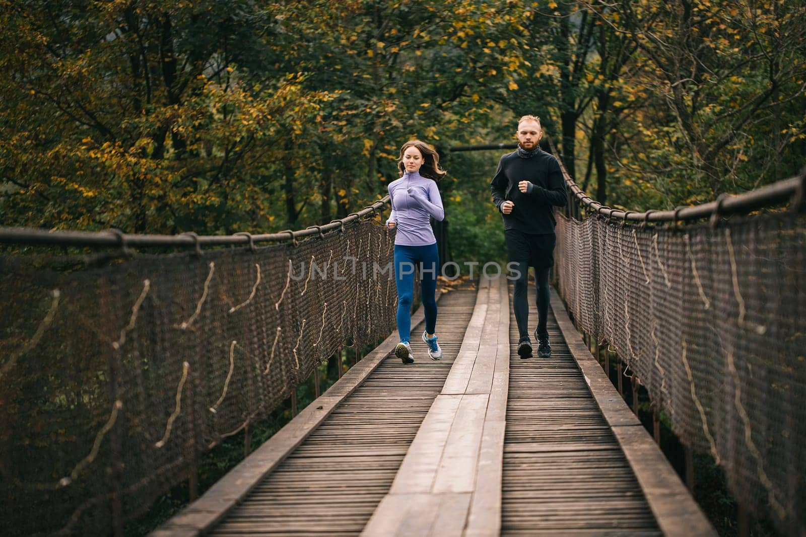 Family spends time with benefit. Loving young sports couple runners running on an old suspension bridge on a cool autumn day. Fitness, sport, people, exercising and lifestyle concept