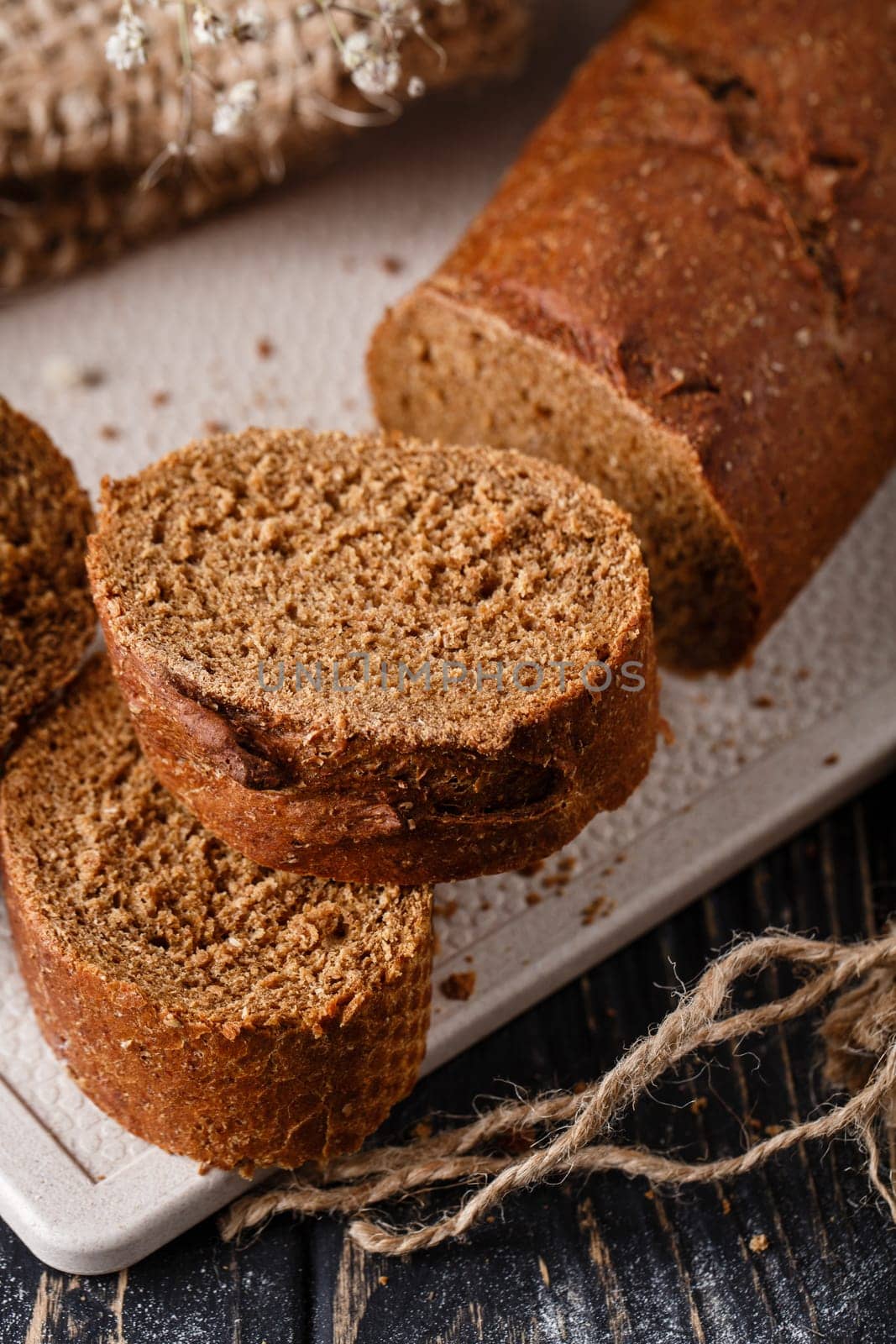 Homemade bread. Slices of freshly baked traditional brown bread with crispy crust. Close up of bread lying on white kitchen board on dark wooden table. Concept of baking bread products.