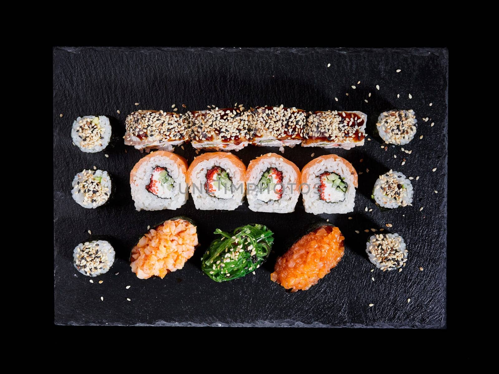 Top view various kinds of sushi served on a dark background. Asian food fest. Menu sushi with nigiri, maki, uramaki on black plate. Japanese restaurant menu.