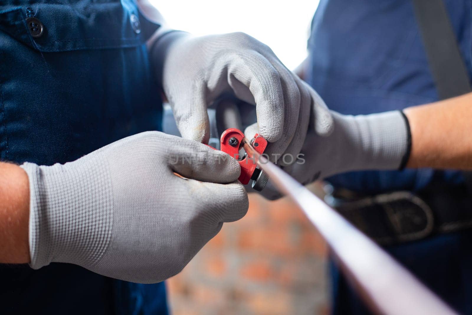 Professional workers in gloves and overalls will prepare pipes when installing heating system in empty apartment. Close up of men winding pipes and cables with insulating tape.