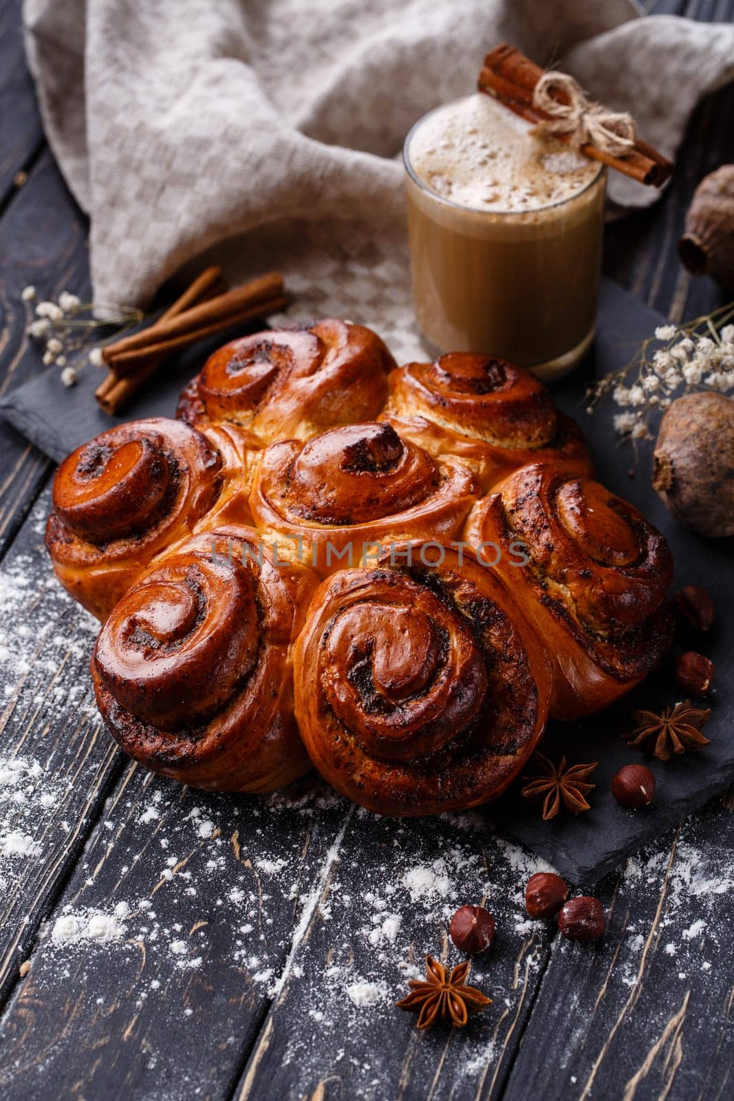 Freshly baked cinnamon buns with spices and stuffing with coffee drink on wooden table. Close up of buns on black methal board on table near Christmas spices. Christmas baking concept.