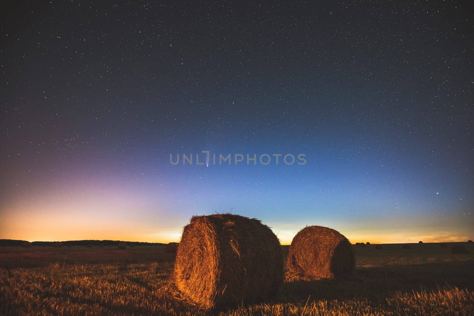 Comet Neowise C2020 F3 In Night Starry Sky Above Haystacks In Summer Agricultural Field. Night Stars Above Rural Landscape With Hay Bales After Harvest. Agricultural Concept.