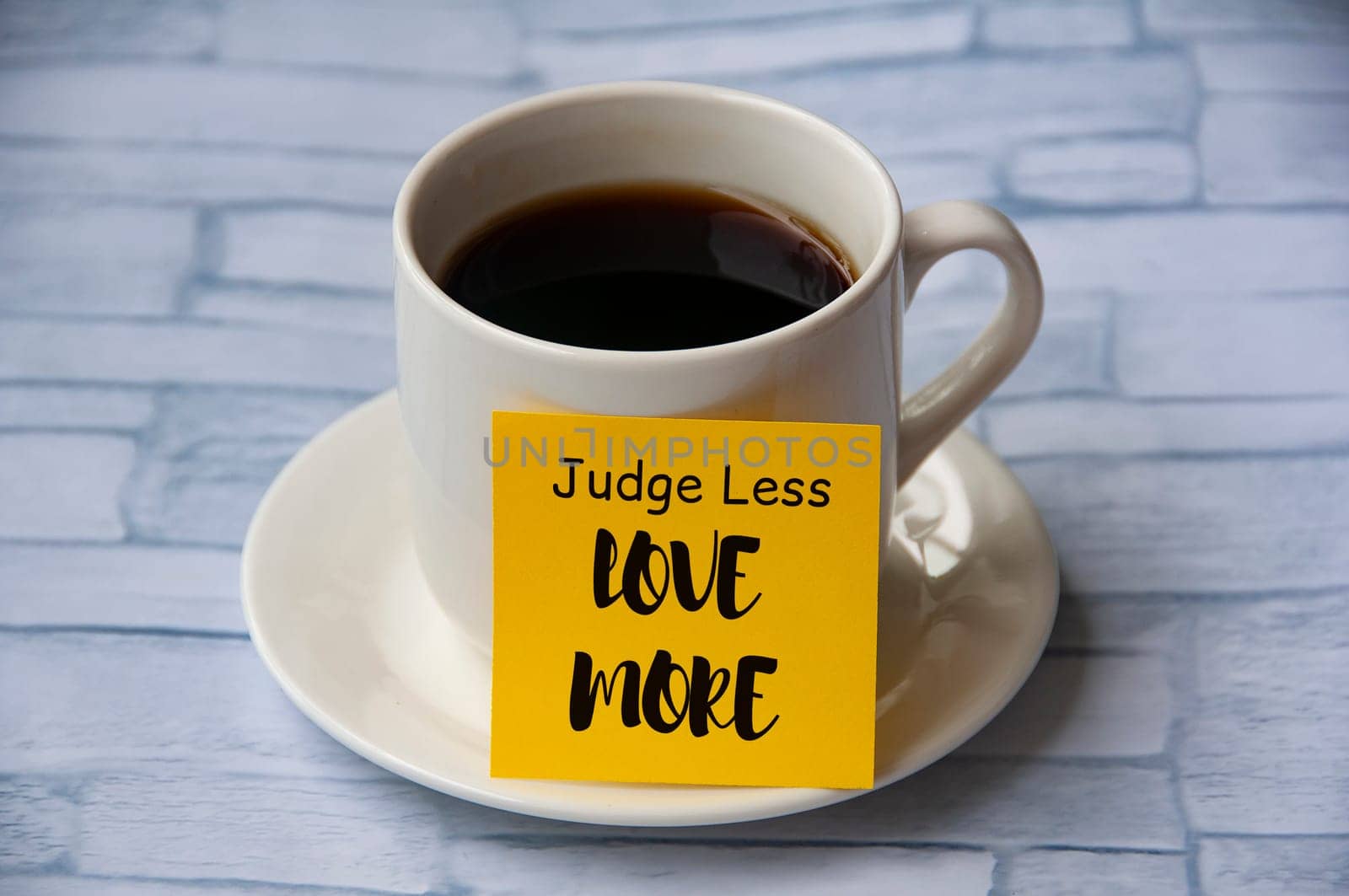 Inspirational quote text on yellow notepad on coffee cup - Judge less love more. Motivational concept.