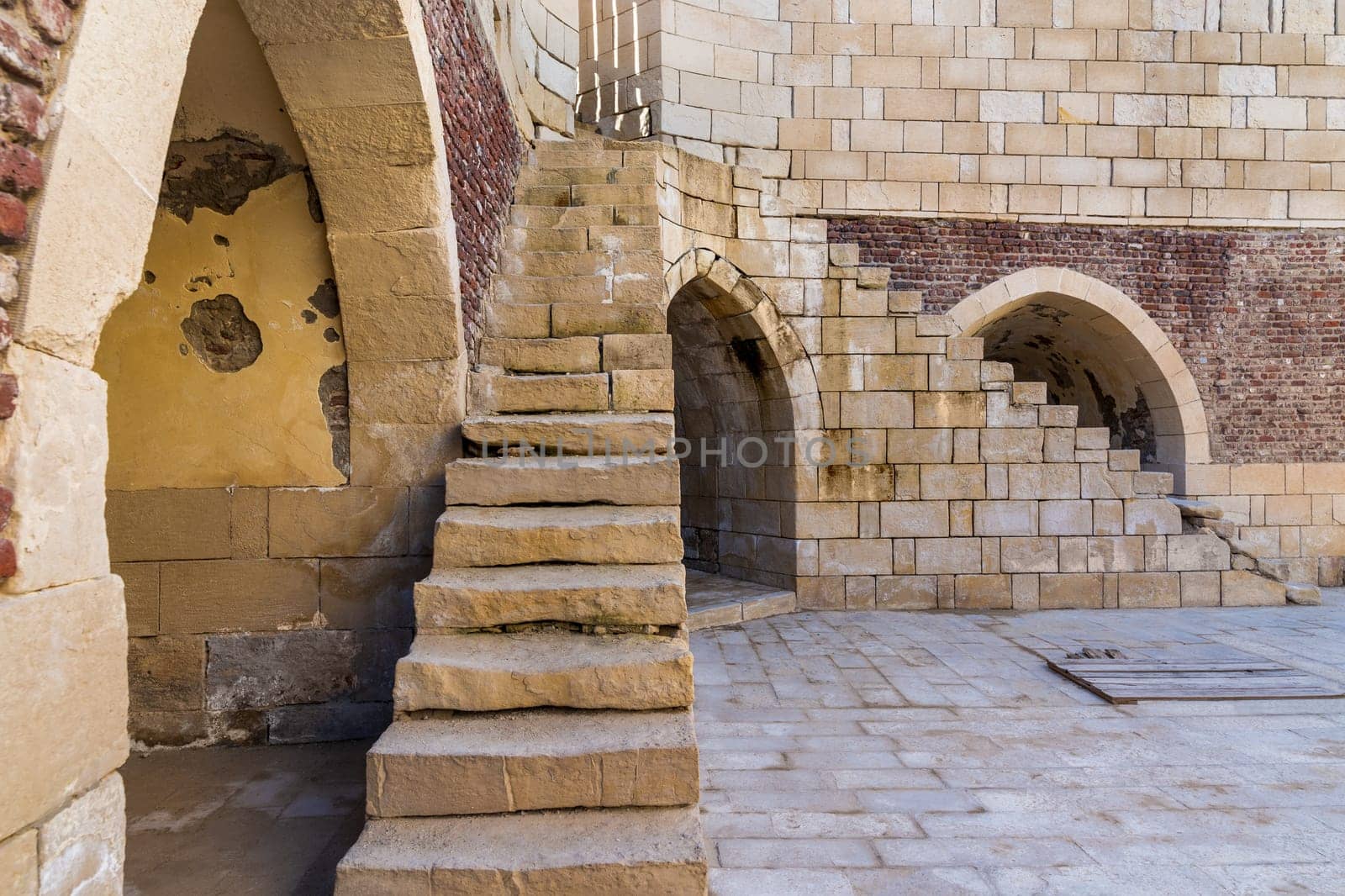 Exterior shot of ancient brick building with two perpendicular shabby stone stairways and two crumbling arched alcoves on street