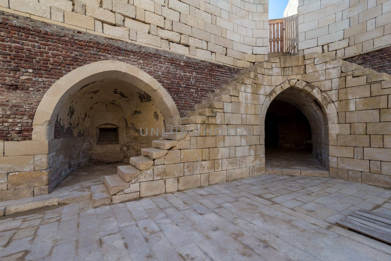 Exterior of ancient brick building with shabby stone stairway and two crumbling arched alcoves on street