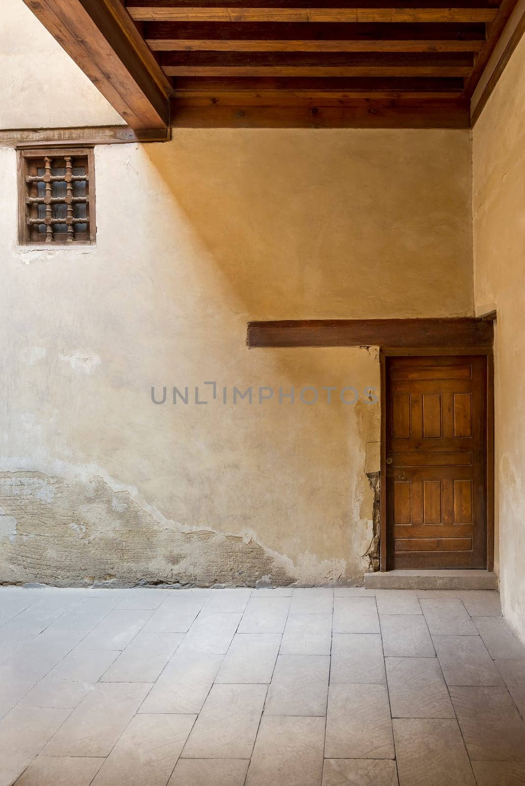 Wooden aged decorated door and small window covered with wooden grid on grunge stone wall and wood timber ceiling