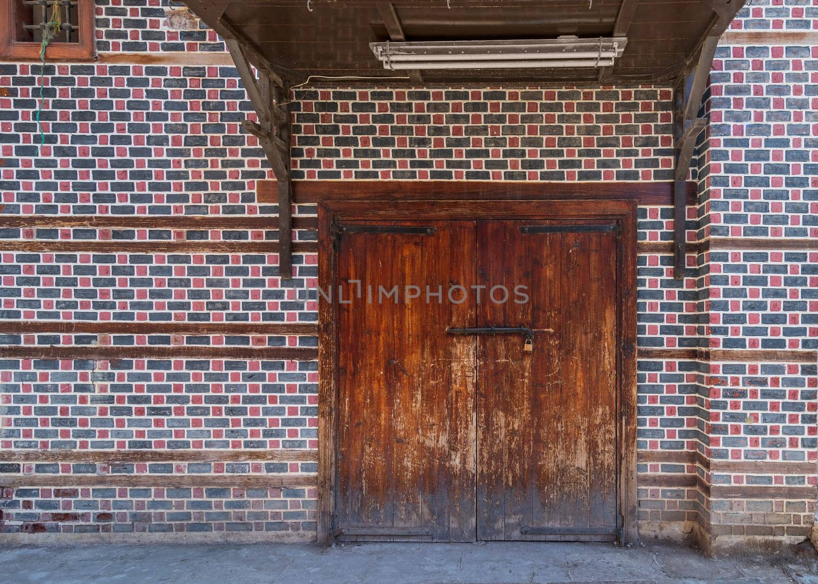 Grunge wooden decorated arched entrance gate with wooden canopy above on wall with black and red bricks with white seam