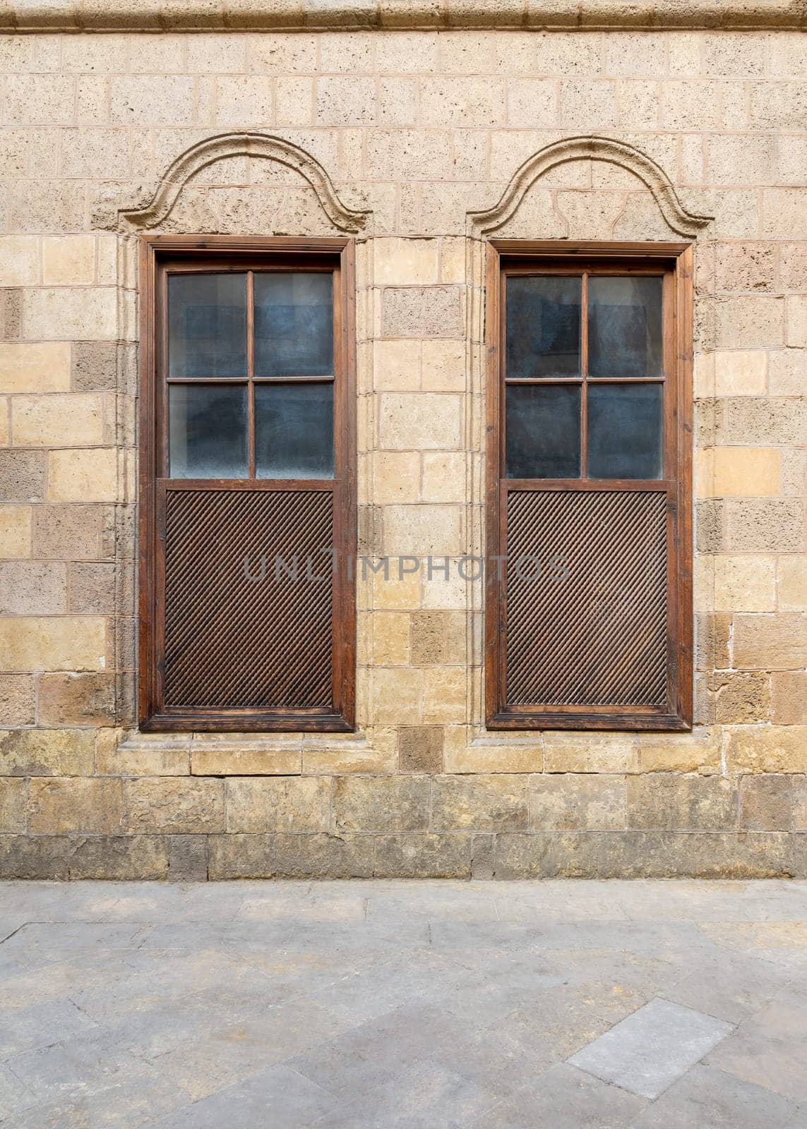 Facade of old abandoned stone decorated bricks wall with two adjacent arched wooden shutter windows