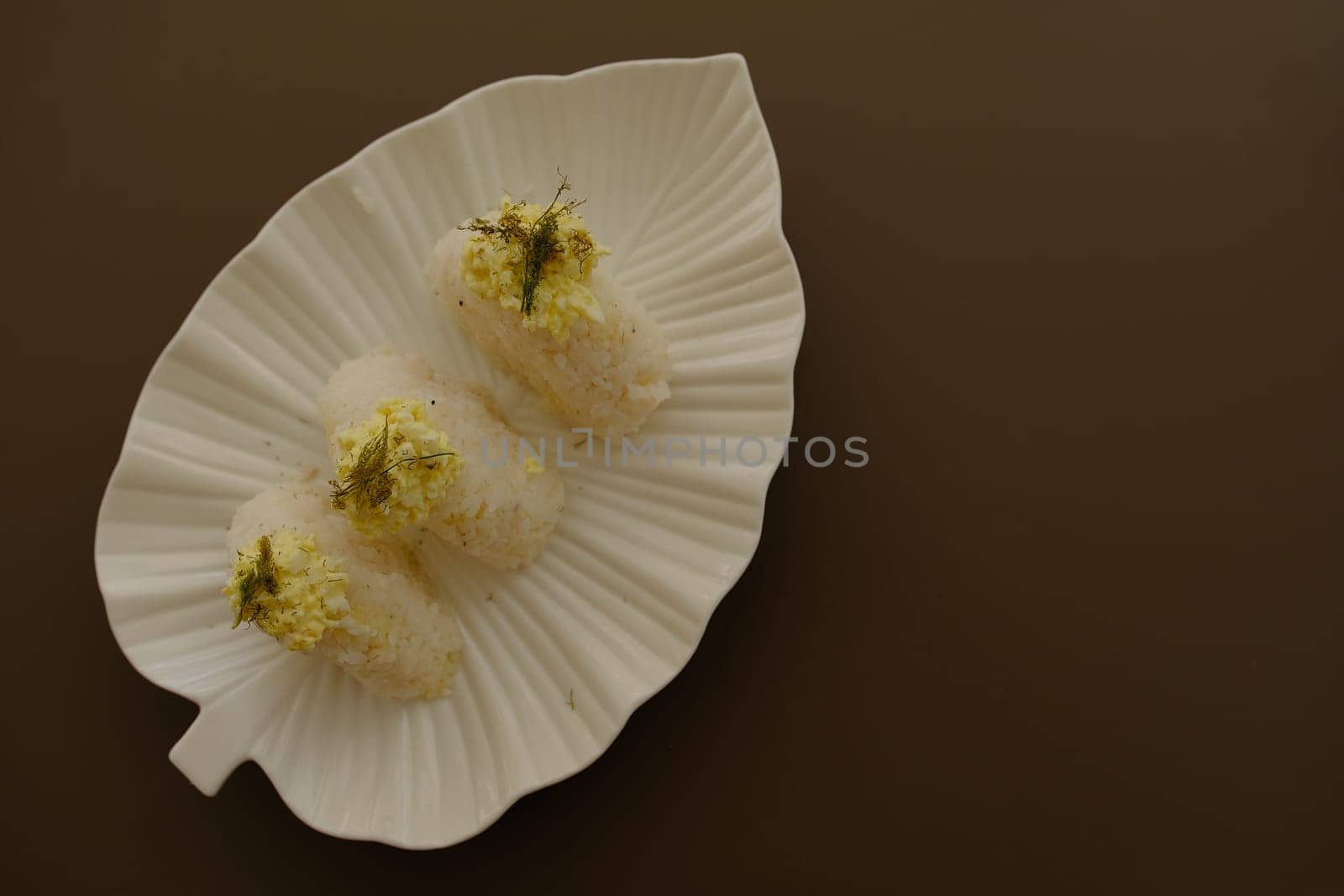 Plate with traditional Japanese onigiri with egg on brown background and beautiful white plate with leaf shape.