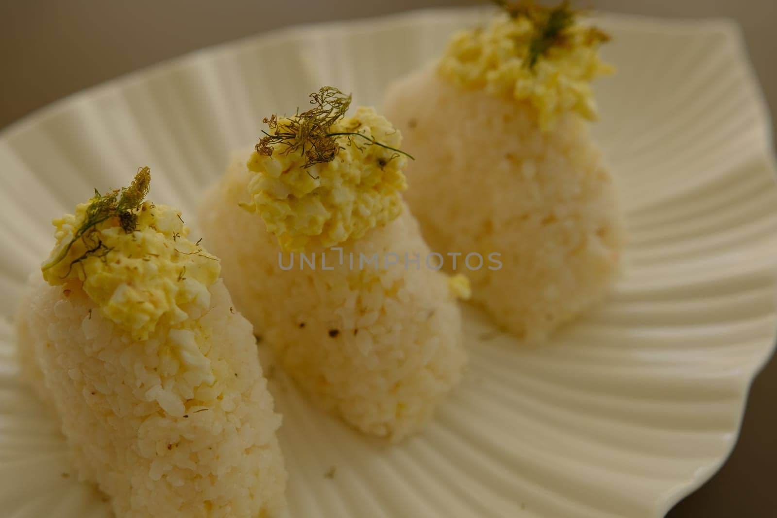 Plate with traditional Japanese onigiri with egg on brown background and beautiful white plate with leaf shape.