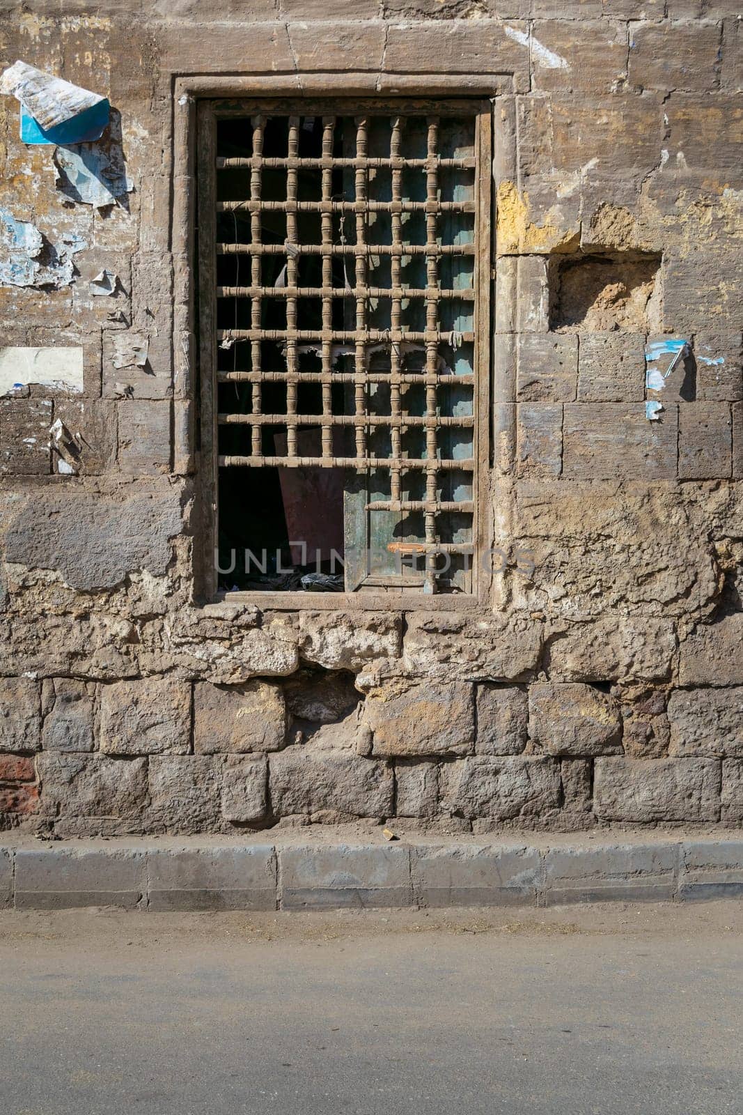 Old abandoned stone bricks wall with one closed grunge broken wooden window covered by wooden grid, Dard El Ahmar district, Cairo, Egypt