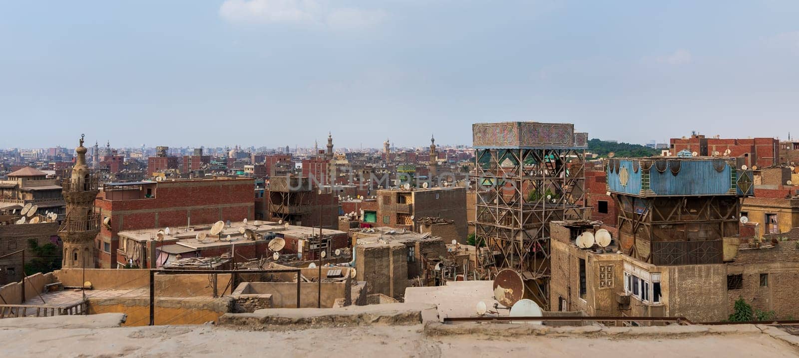 Shabby buildings with satellite dishes on rooftops located against blue sky in ancient city of Cairo, Egypt