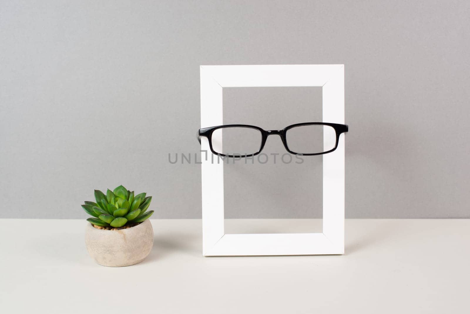 Home interior poster mock up with wooden frame, eyeglasses and cactus in a pot, gray wall background, copy space for text and pictures