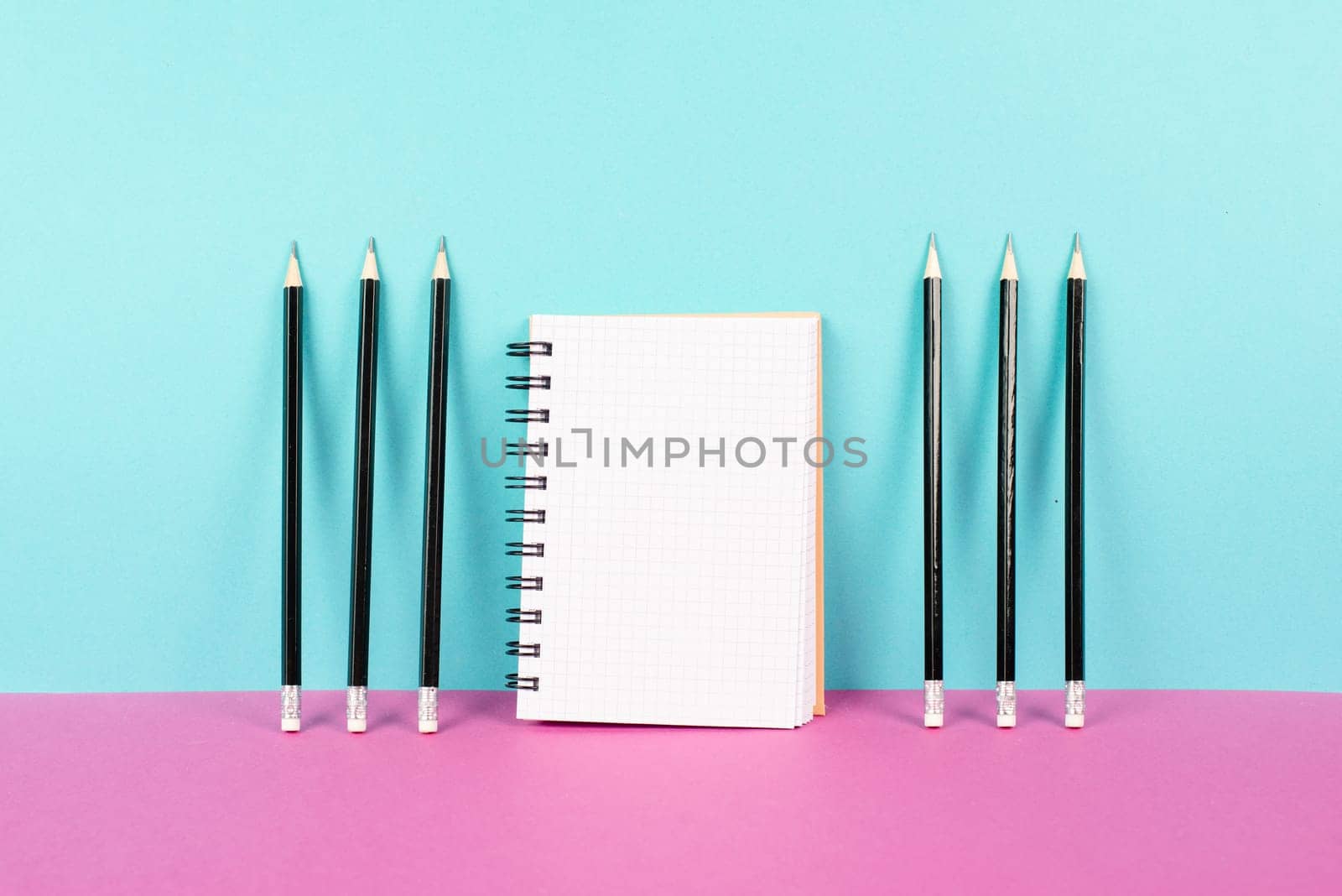 Empty notebook with a pencils on a pink and blue background, brainstorming for new ideas, writing a message, home office desk