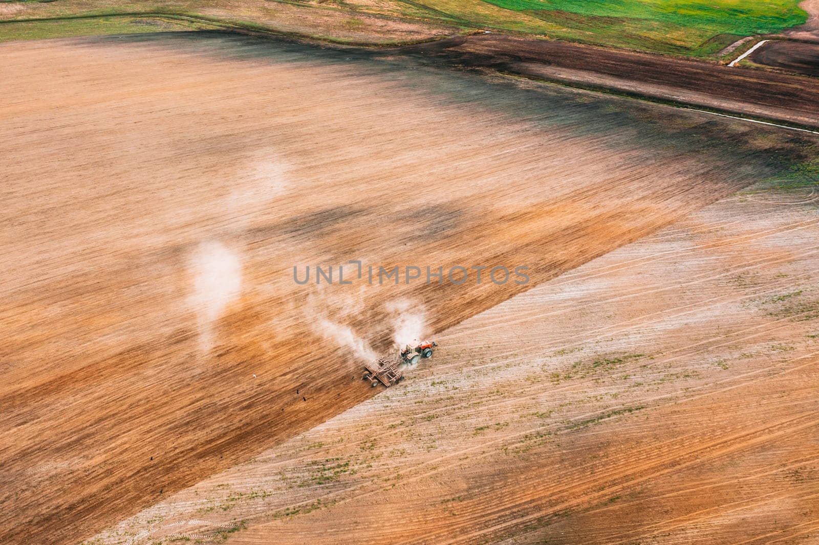 Aerial View. Tractor Plowing Field In Spring Season. Beginning Of Agricultural Spring Season. Cultivator Pulled By A Tractor In Countryside Rural Field Landscape.