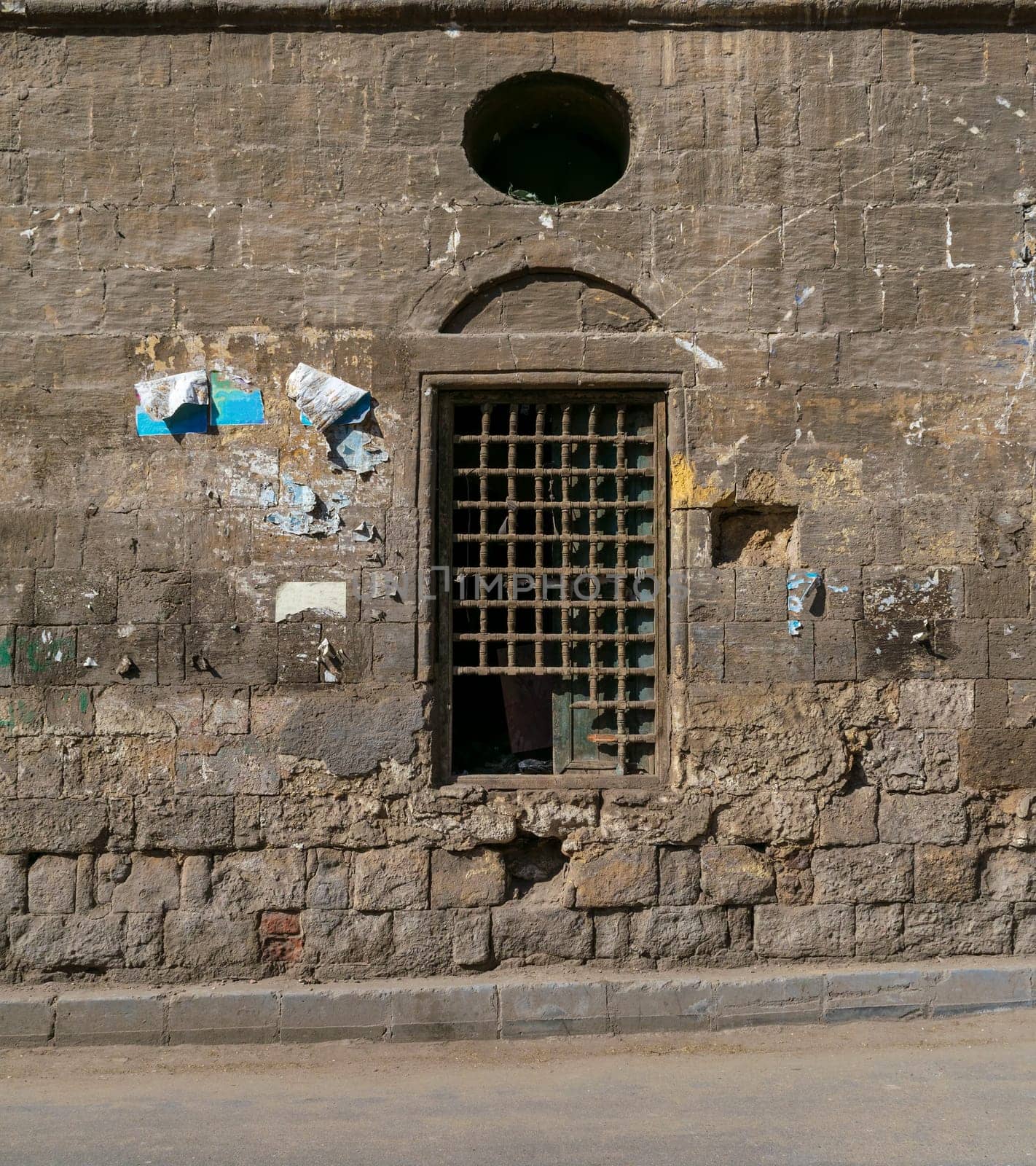 Old abandoned stone bricks wall with one closed grunge broken wooden window covered by wooden grid, Dard El Ahmar district, Cairo, Egypt