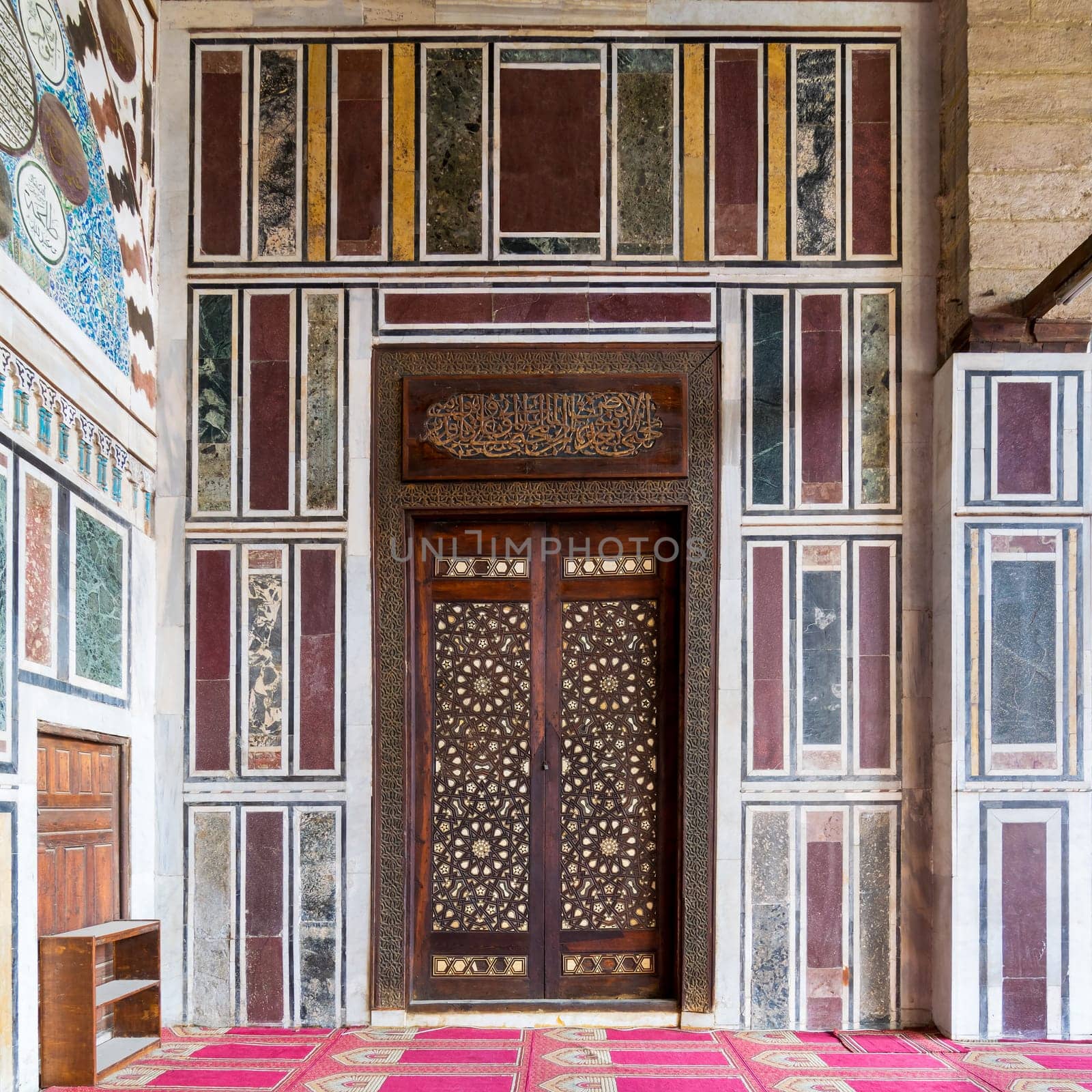 Old colorful marble wall with wooden door decorated with arabesque ornaments in public historic Al Moaayad Mosque, Cairo, Egypt