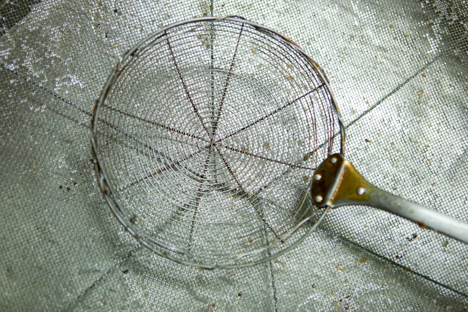 Skimmer driping oil over sieve. Used for cooking with fried food