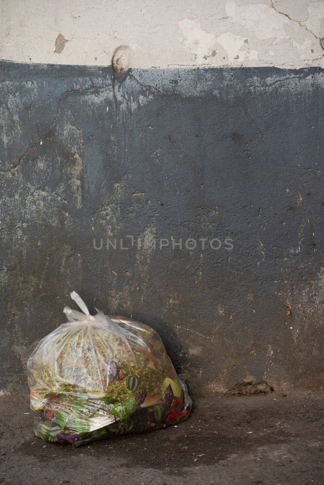 Plastic bag full of trash in front of dirty wall