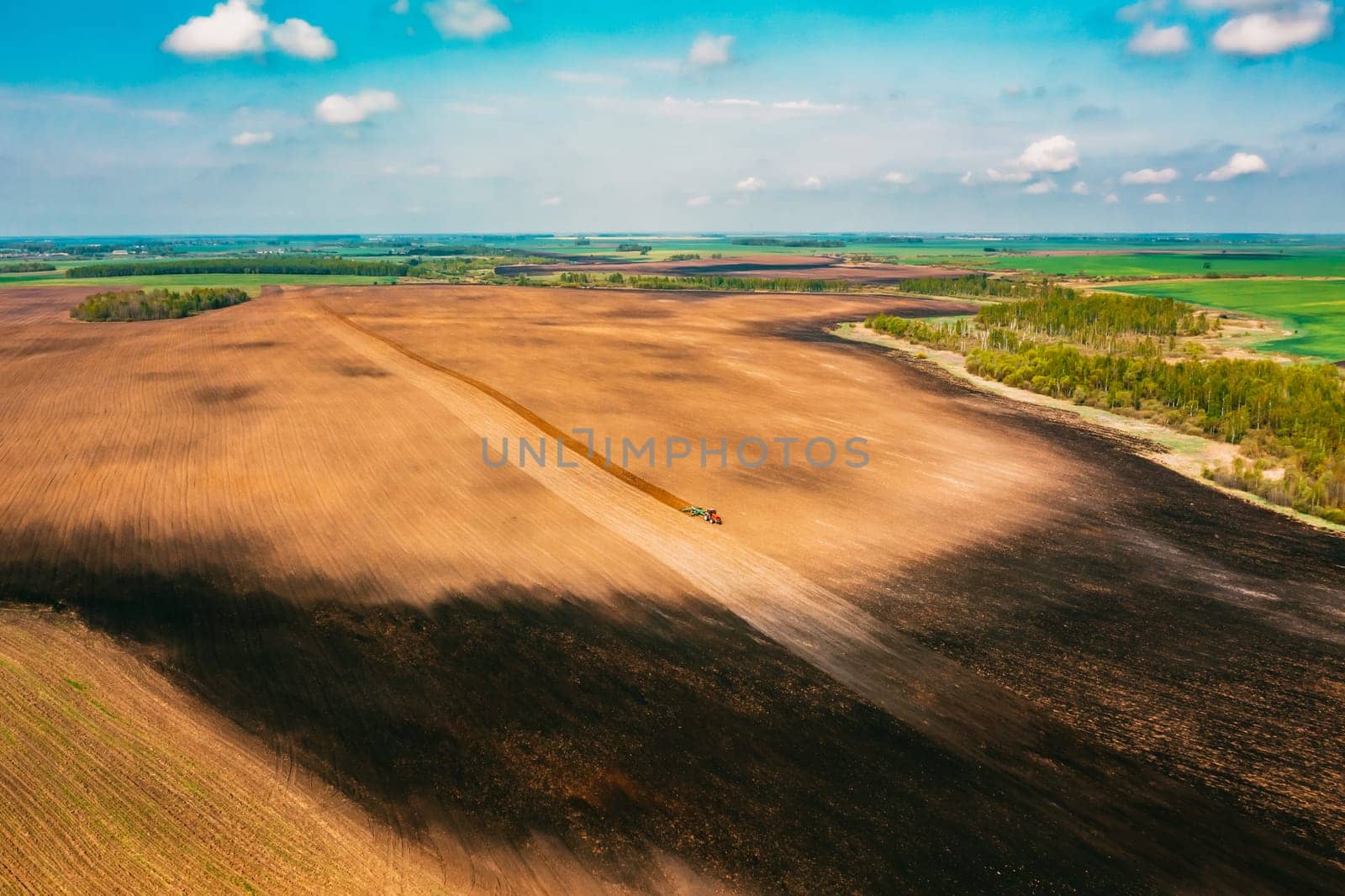 Aerial View. Tractor Plowing Field In Spring Season. Beginning Of Agricultural Spring Season. Cultivator Pulled By A Tractor In Countryside Rural Field Landscape.