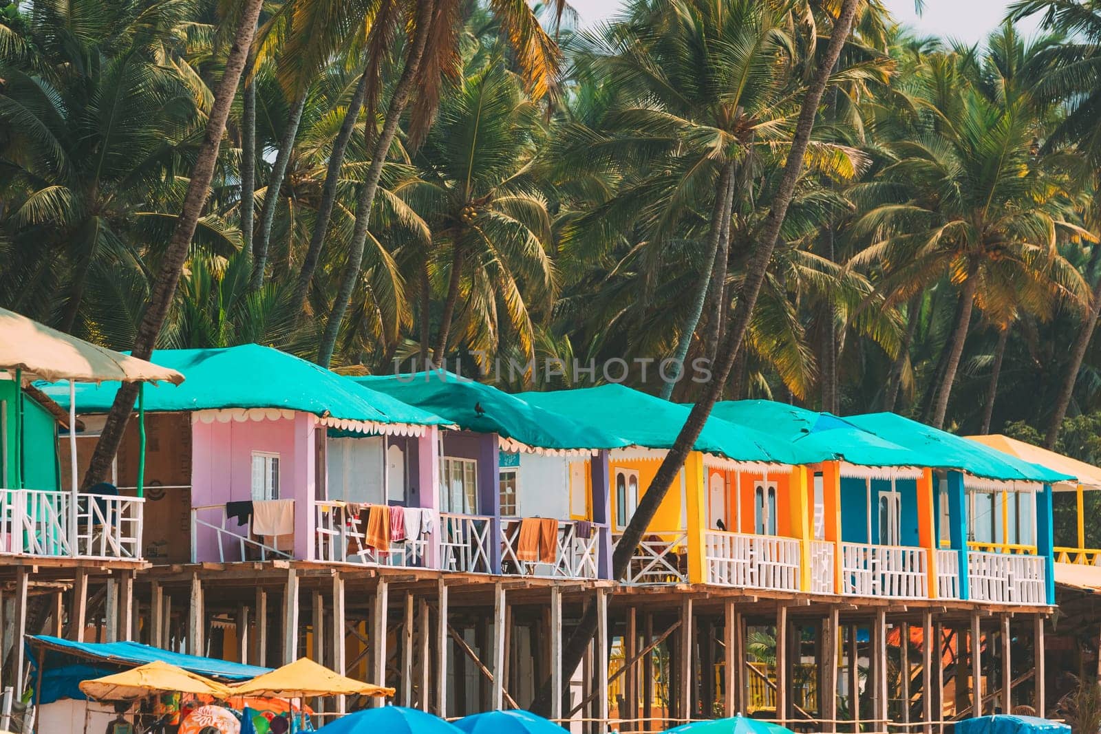 Canacona, Goa, India. Famous Painted Guest Houses On Palolem Beach Against Background Of Tall Palm Trees In Sunny Day.