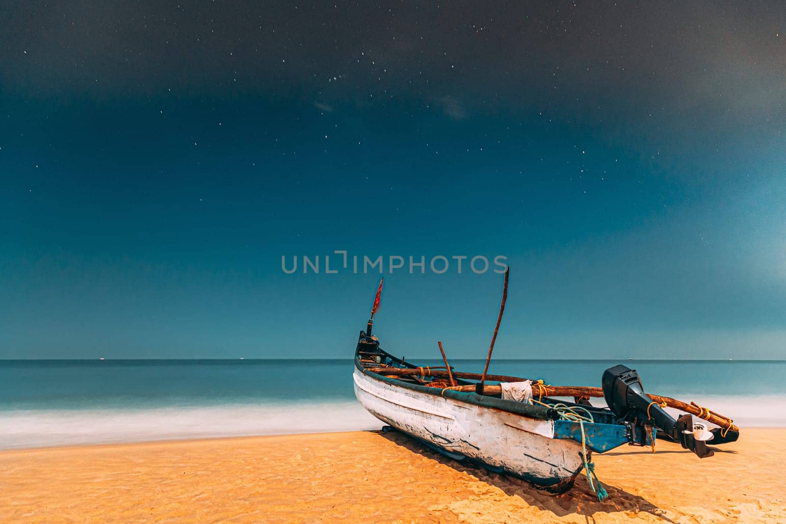 Goa, India. Real Night Sky Stars. Natural Starry Sky Blue Color Above Sea Seascape Ocean Beach. Background. Parked Old Wooden Boat At Coast.
