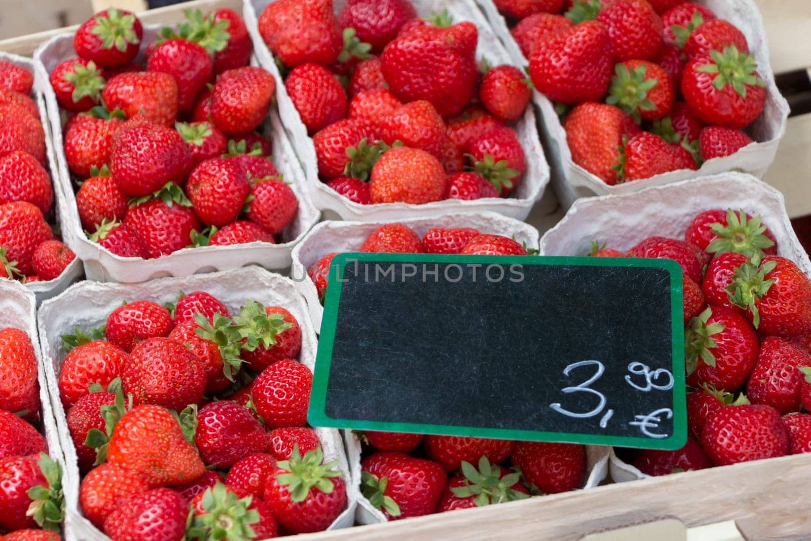 Cups of fresh sweet quality strawberries at marketplace. Local bio fruit sale with euro price tag and blank black label copyspace.