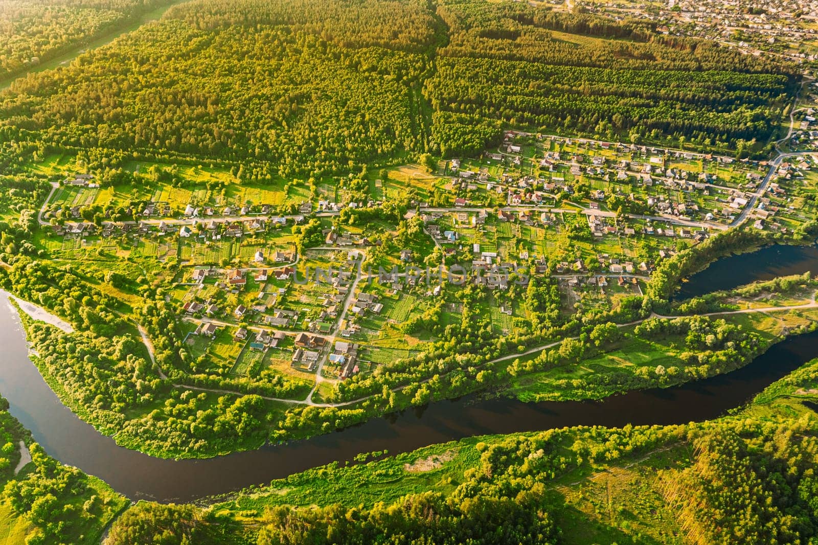 Aerial View Of Calm River And Village In Belarus, Europe. Green Forest Woods Landscape In Sunny Summer Evening. Top View Of Beautiful European Nature From High Attitude. Drone View. Bird's Eye View.