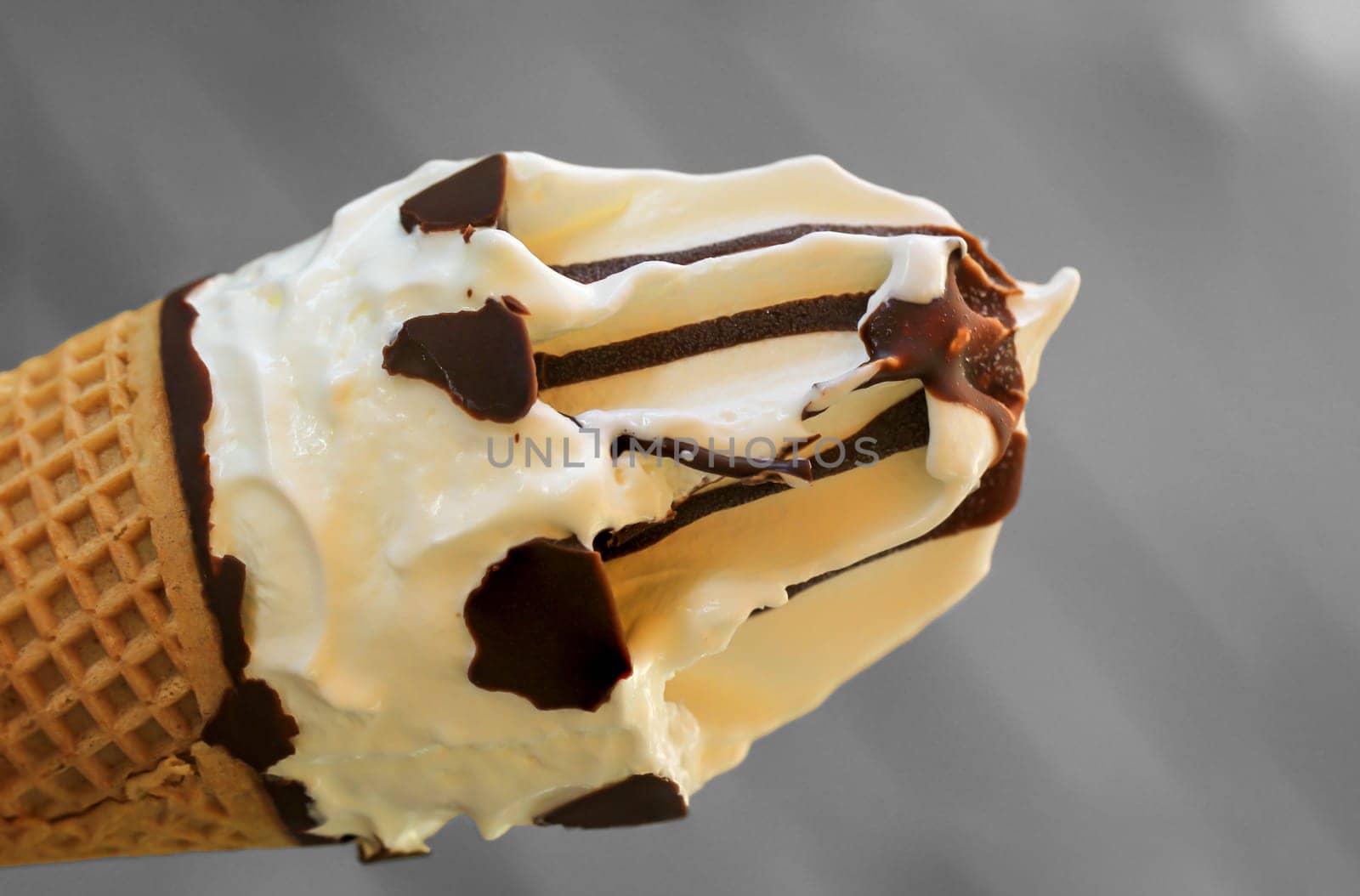A close up of an ice cream cone with vanilla ice cream and chocolate icing.