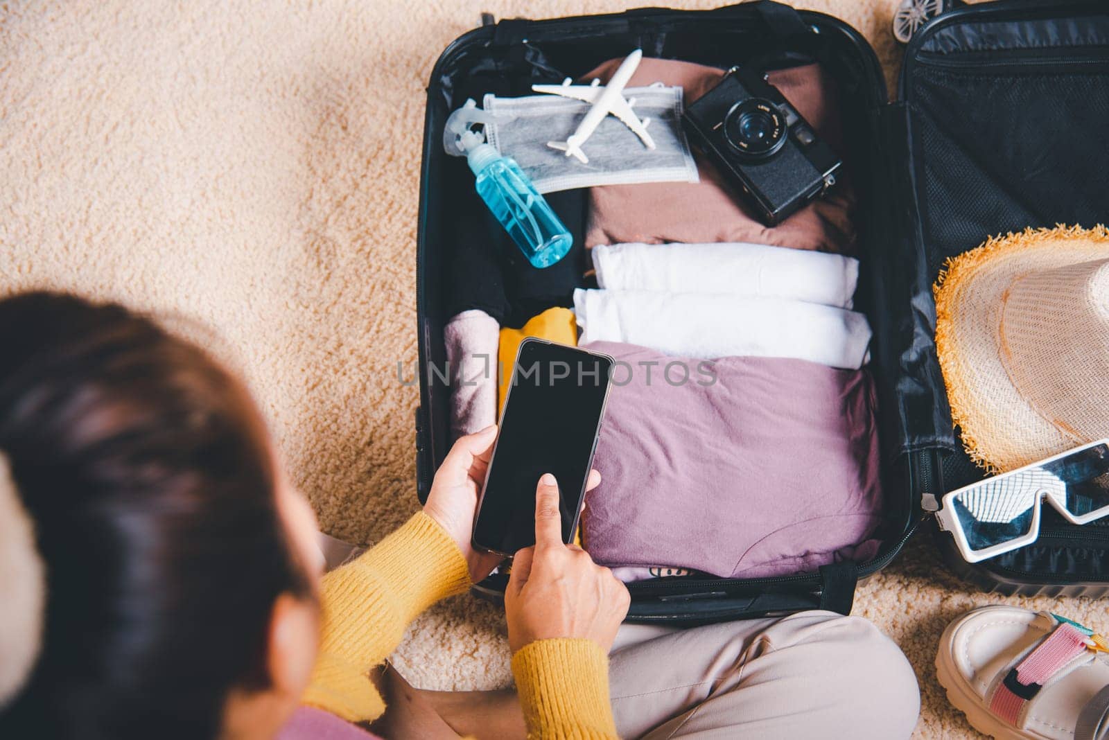 Woman using smartphone blank screen and packing suitcase bag for travel trip weekend vacation at home, female check information in tourism website on mobile phone before go to airport