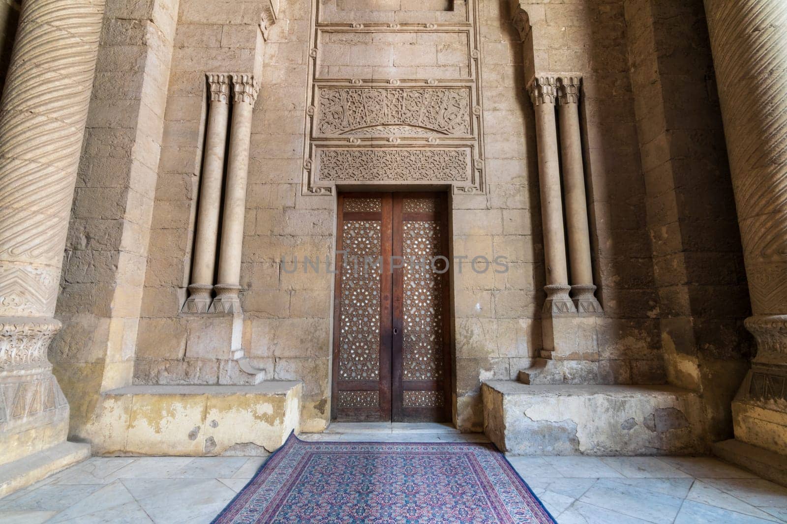 External old decorated bricks stone wall with arabesque decorated wooden door framed by stone ornate cylindrical columns leading to al Rifai Mosque, Old Cairo, Egypt