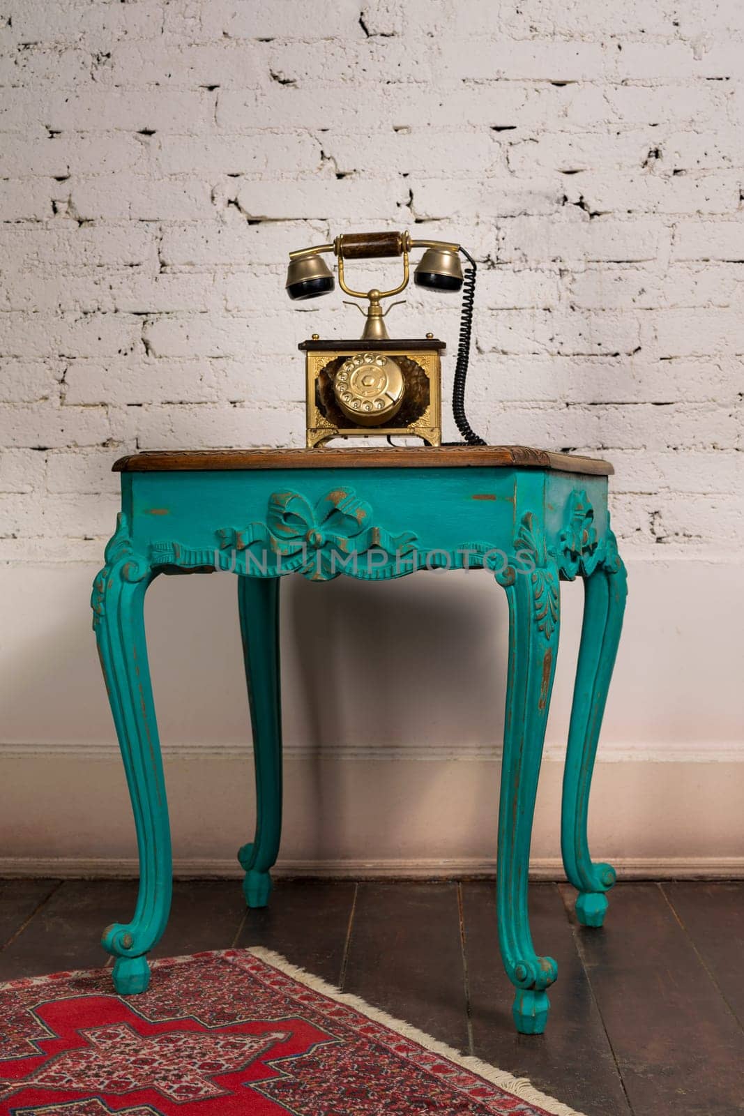 Retro composition of green vintage wooden table and old golden telephone set on a background of red carpet, dark brown wooden floor and white bricks wall