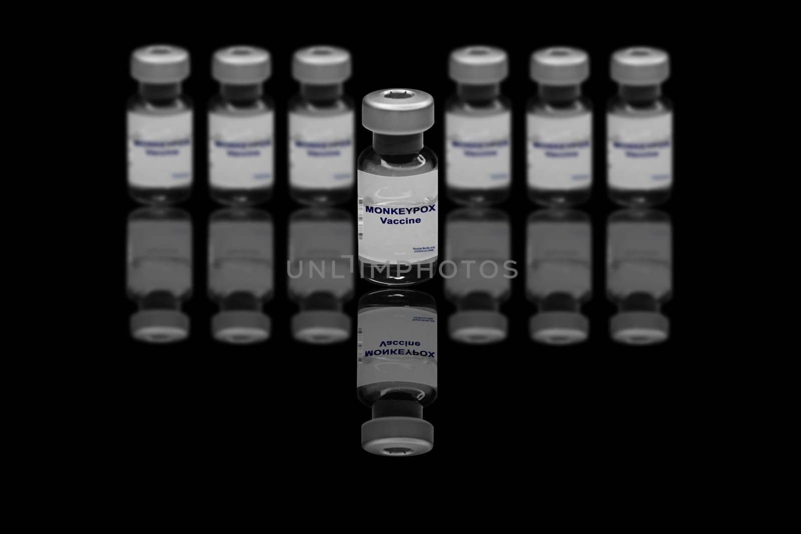 Monkeypox vaccine close-up on a black mirror background. In the background are blurred vaccine vials.